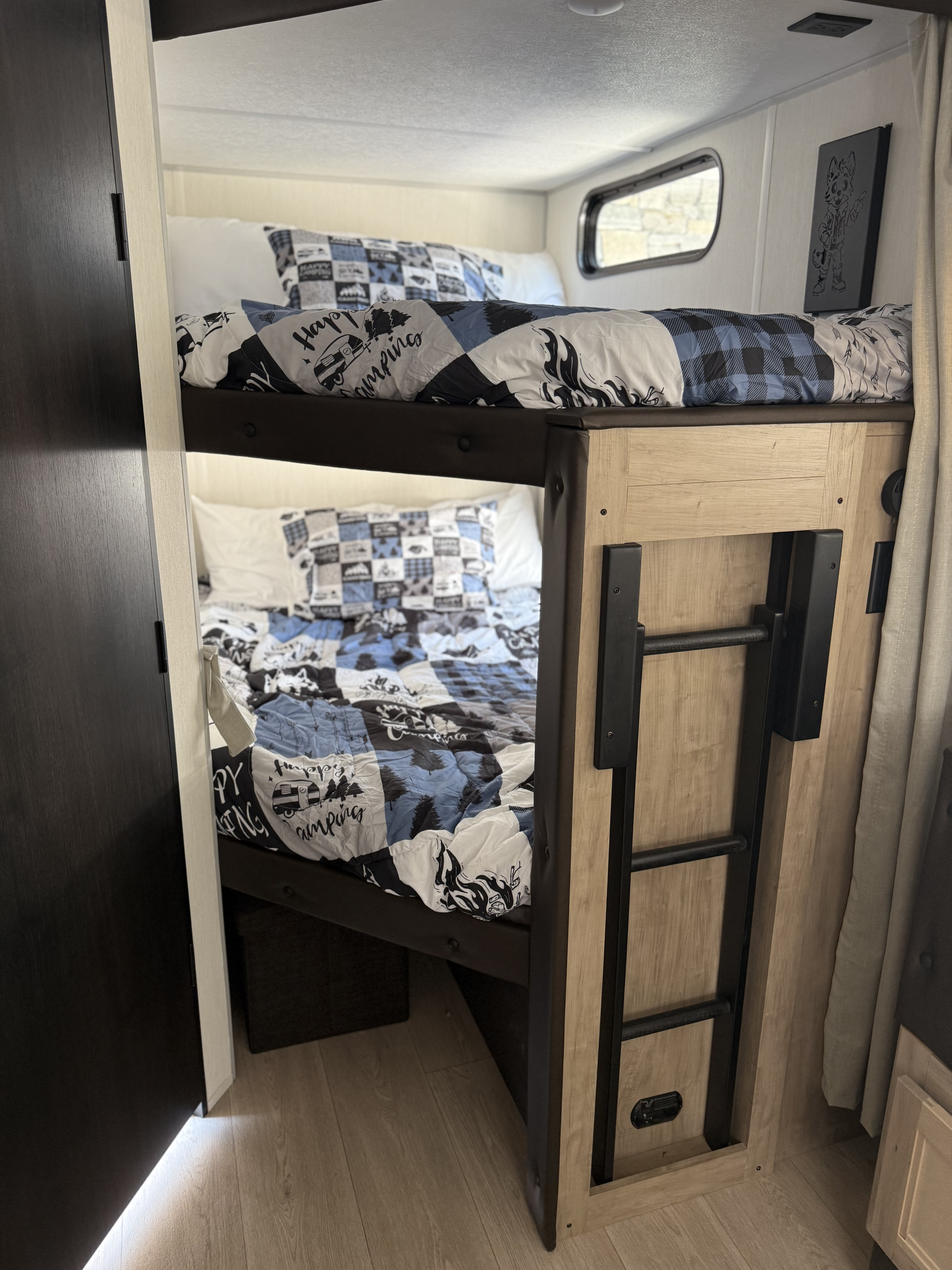 Inside an rv rental, two bunk beds feature blue, black, and white camping-themed bedding. A ladder provides access to the top bunk.. Forest River Grey wolf 2026