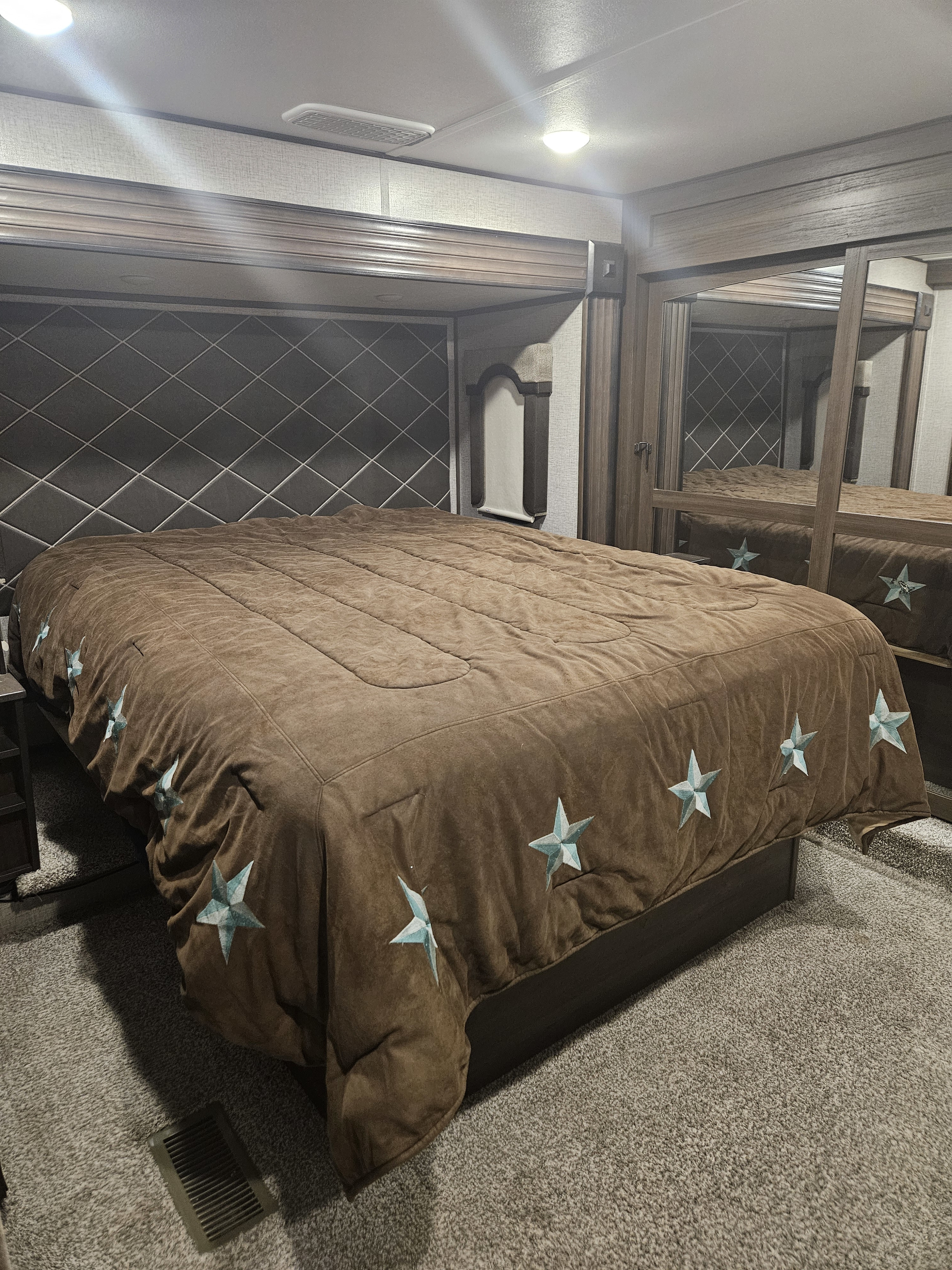 Cozy RV rental bedroom featuring a large bed with a brown, star-decorated comforter, a padded headboard, and mirrored wardrobe.. Keystone RV Avalanche 2020