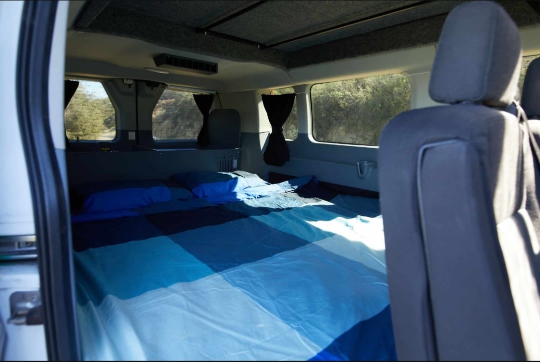 Cozy RV rental interior: A blue-themed bed fills the rear, visible from the side door, with natural light through windows.. Ford Transit 2017