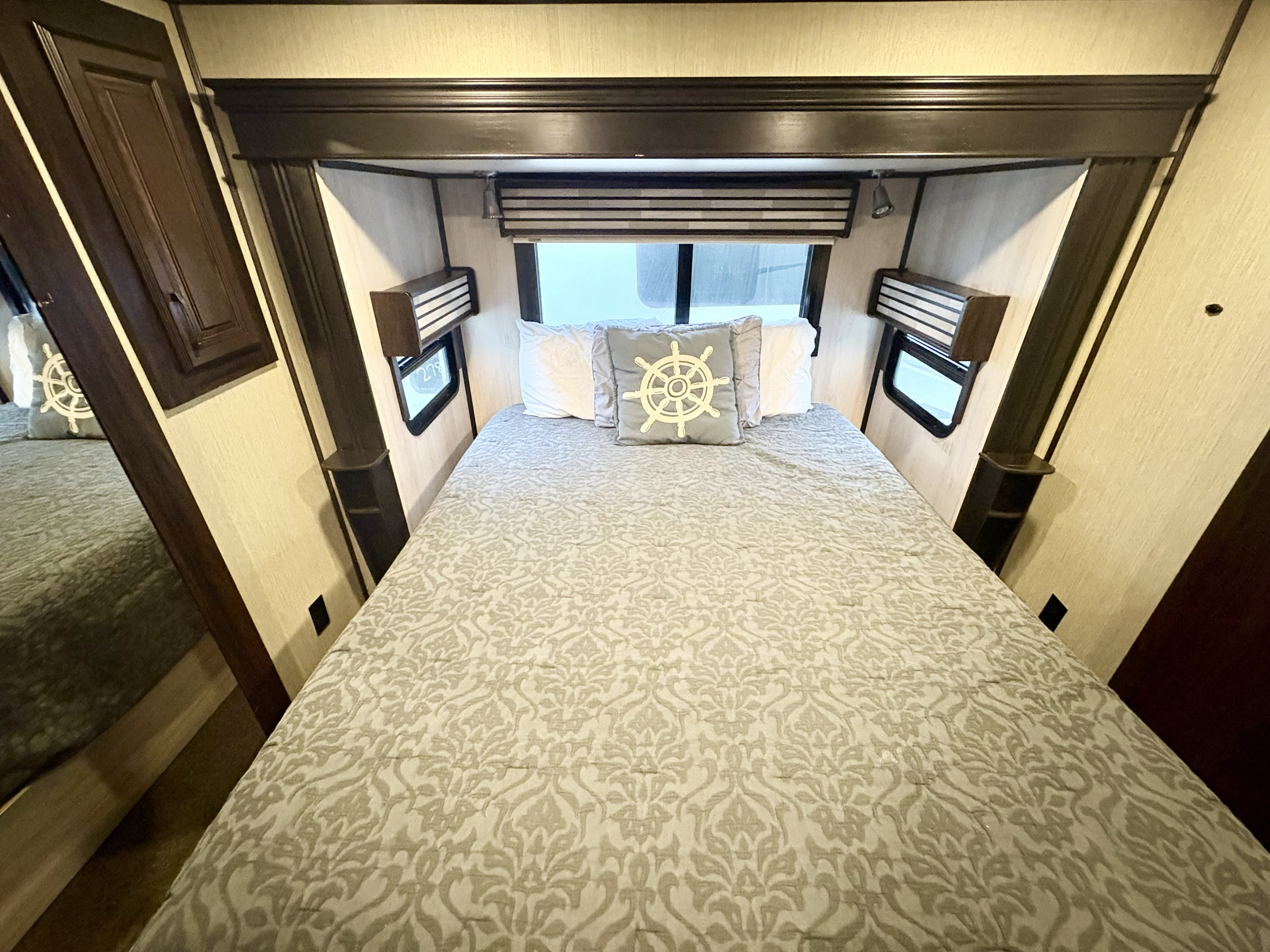 Cozy RV rental bedroom featuring a neatly made bed with ship's wheel pillow, windows, and built-in storage.. Forest River Palomino Columbus 2018