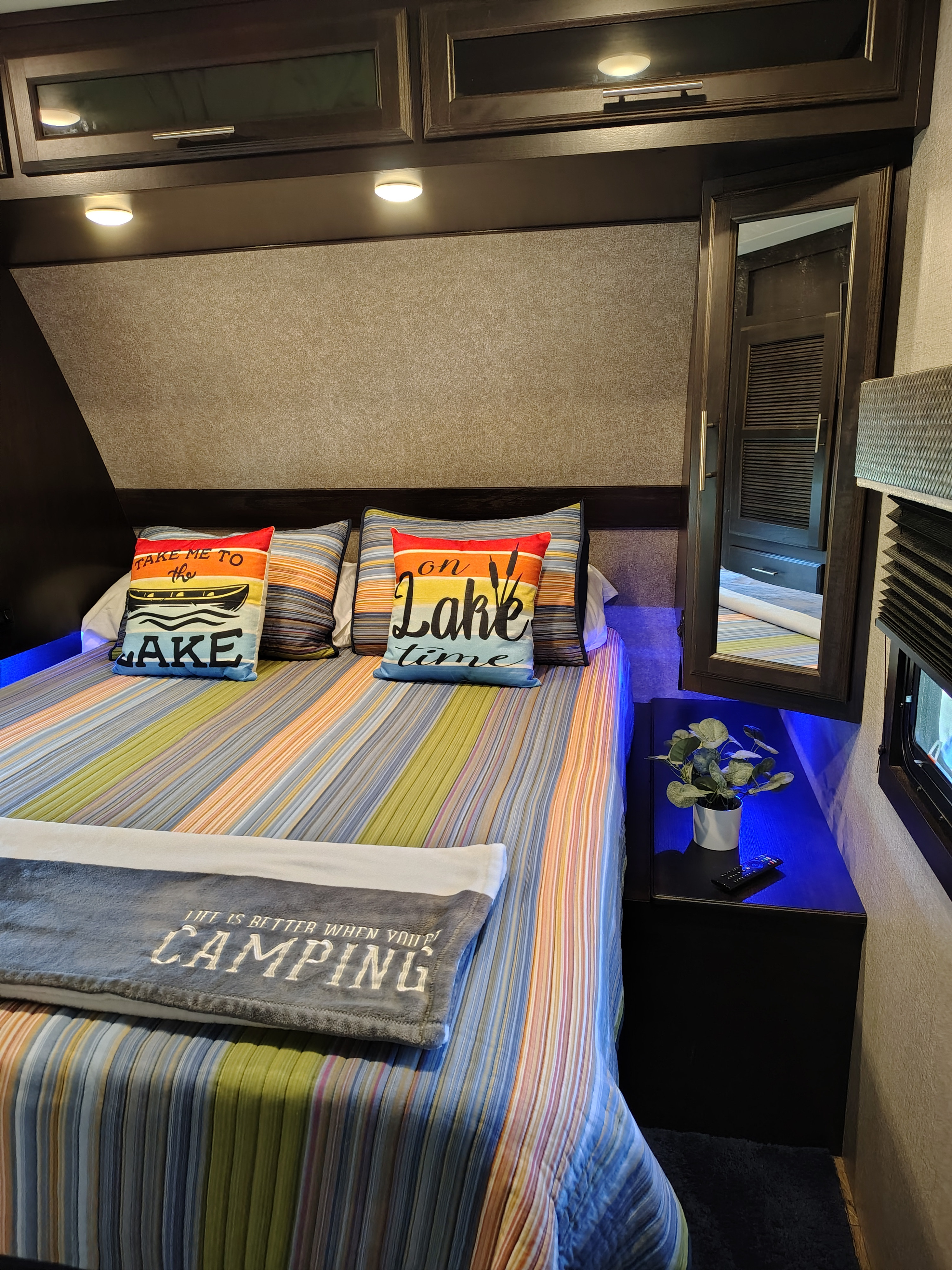 Cozy RV rental bedroom featuring a striped bed, lake pillows, a camping blanket, and cool blue accent lights.. Jayco Eagle HT 2021