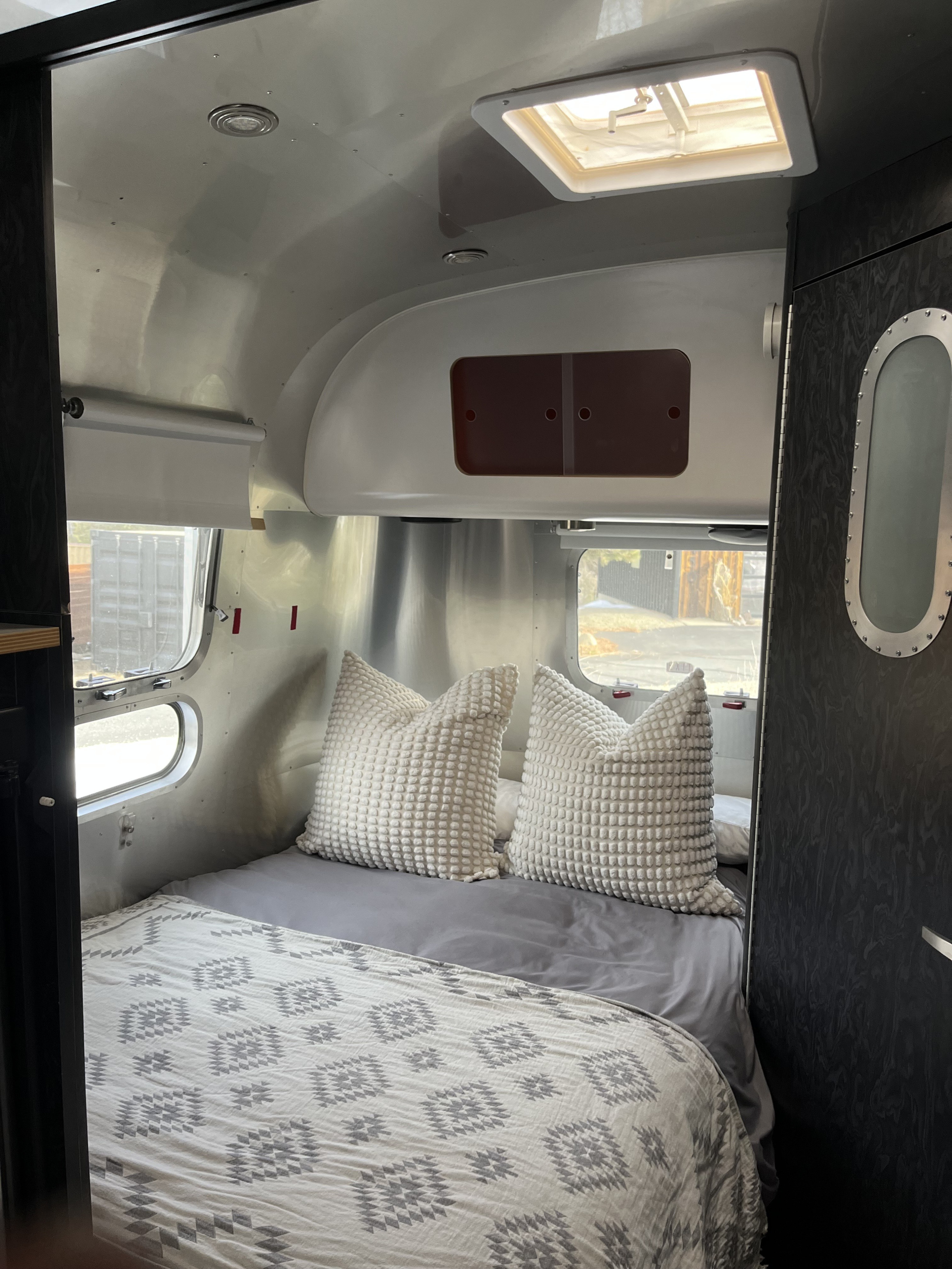 Inside a cozy Airstream rv rental bedroom. Features a bed with patterned quilt, textured pillows, a window, and a skylight.. Airstream Bambi International 2006