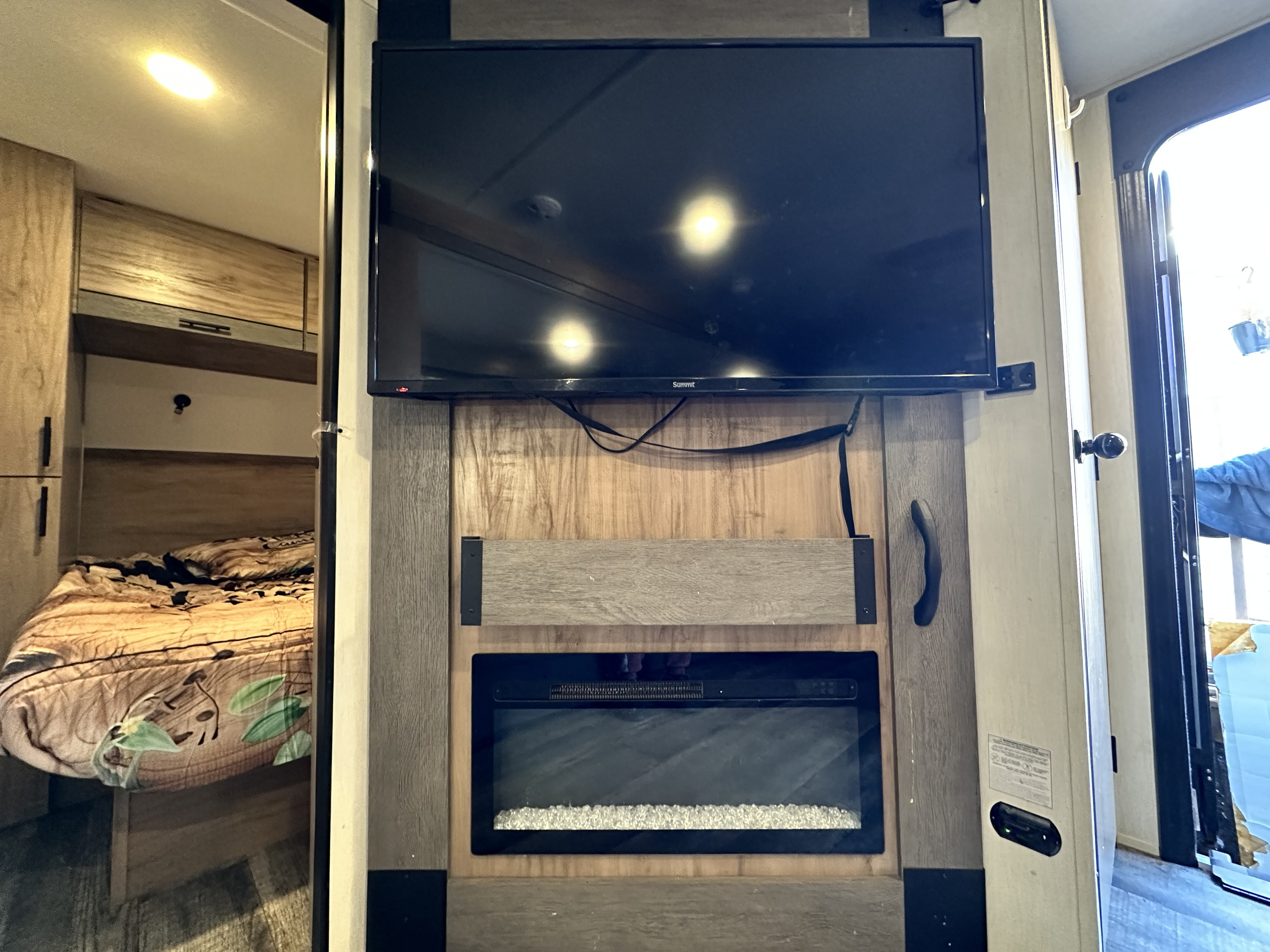 Cozy RV rental interior featuring a TV, electric fireplace, and compact bedroom area with patterned bedding.. Forest River Campsite Reserve 2025