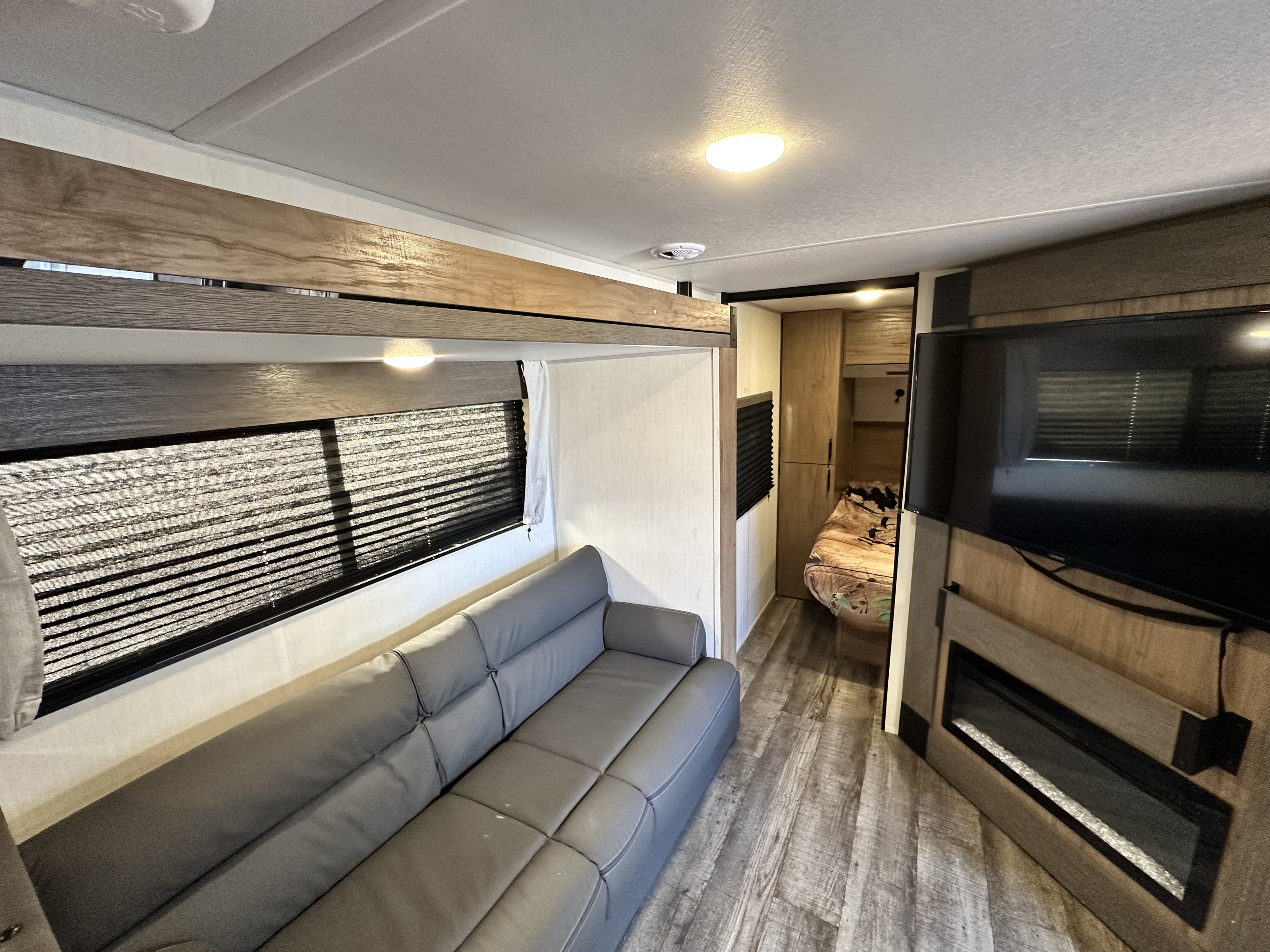 Modern RV rental interior featuring a comfy gray couch, bunk bed, TV, electric fireplace, and a peek into the bedroom.. Forest River Campsite Reserve 2025