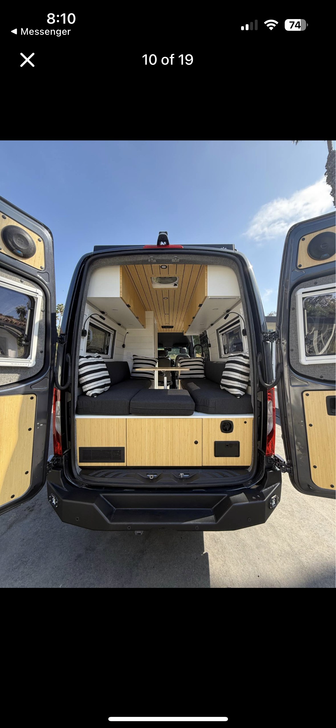 RV rental: Modern camper van interior with open back doors, featuring a seating/bed area, table, and wood accents.. Mercedes Sprinter 2022