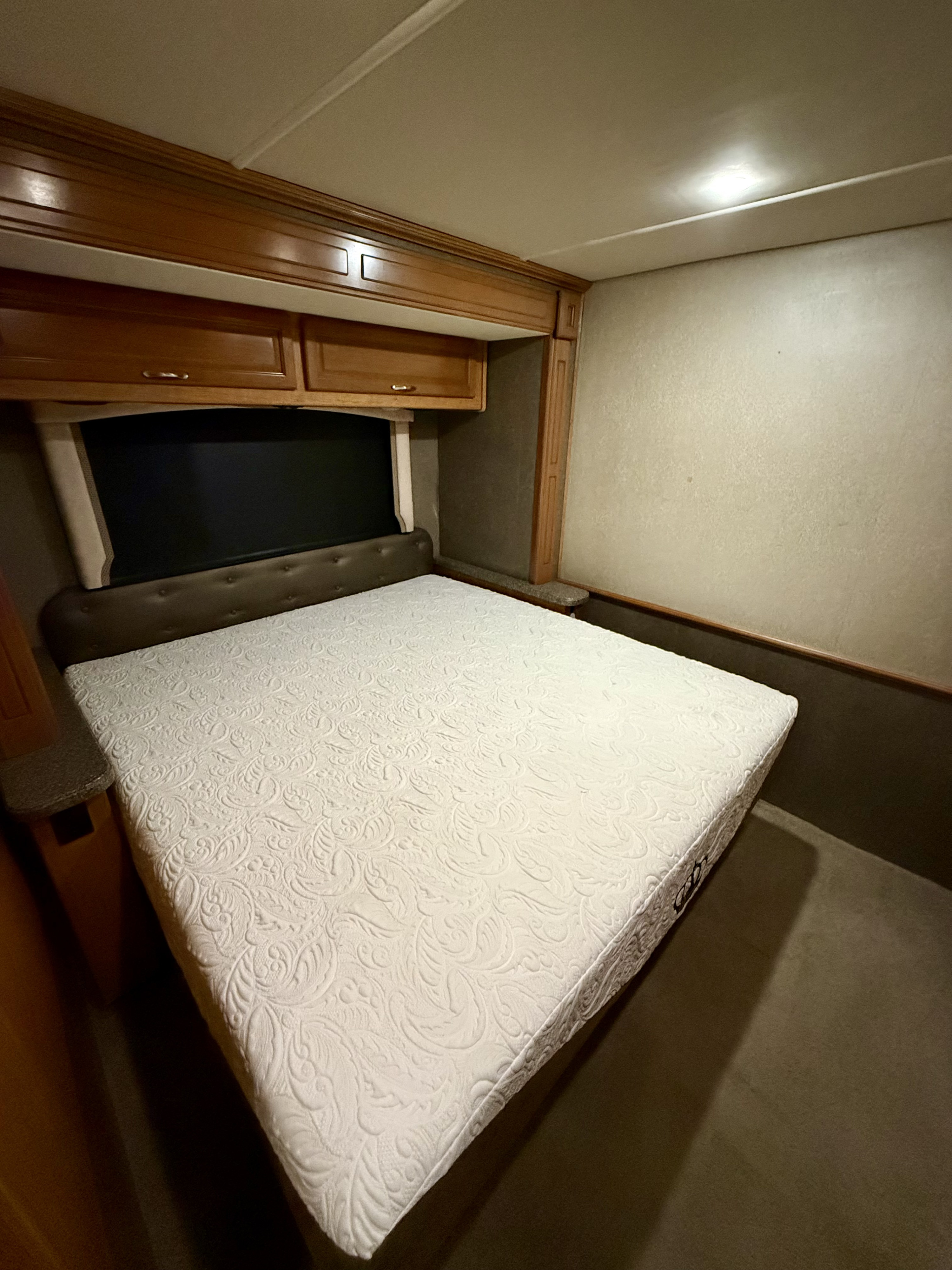 Clean RV rental bedroom with a white mattress, dark headboard, and wood cabinets, ready for comfortable rest.. Fleetwood Bounder 33C 2016