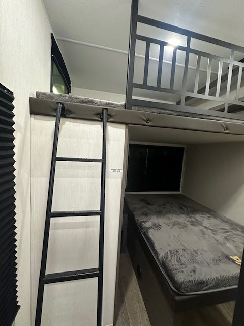 Cozy RV rental interior featuring a bunk bed setup with a ladder leading to the upper bunk and a lower bed.. Forest River Cherokee Arctic Wolf 2025