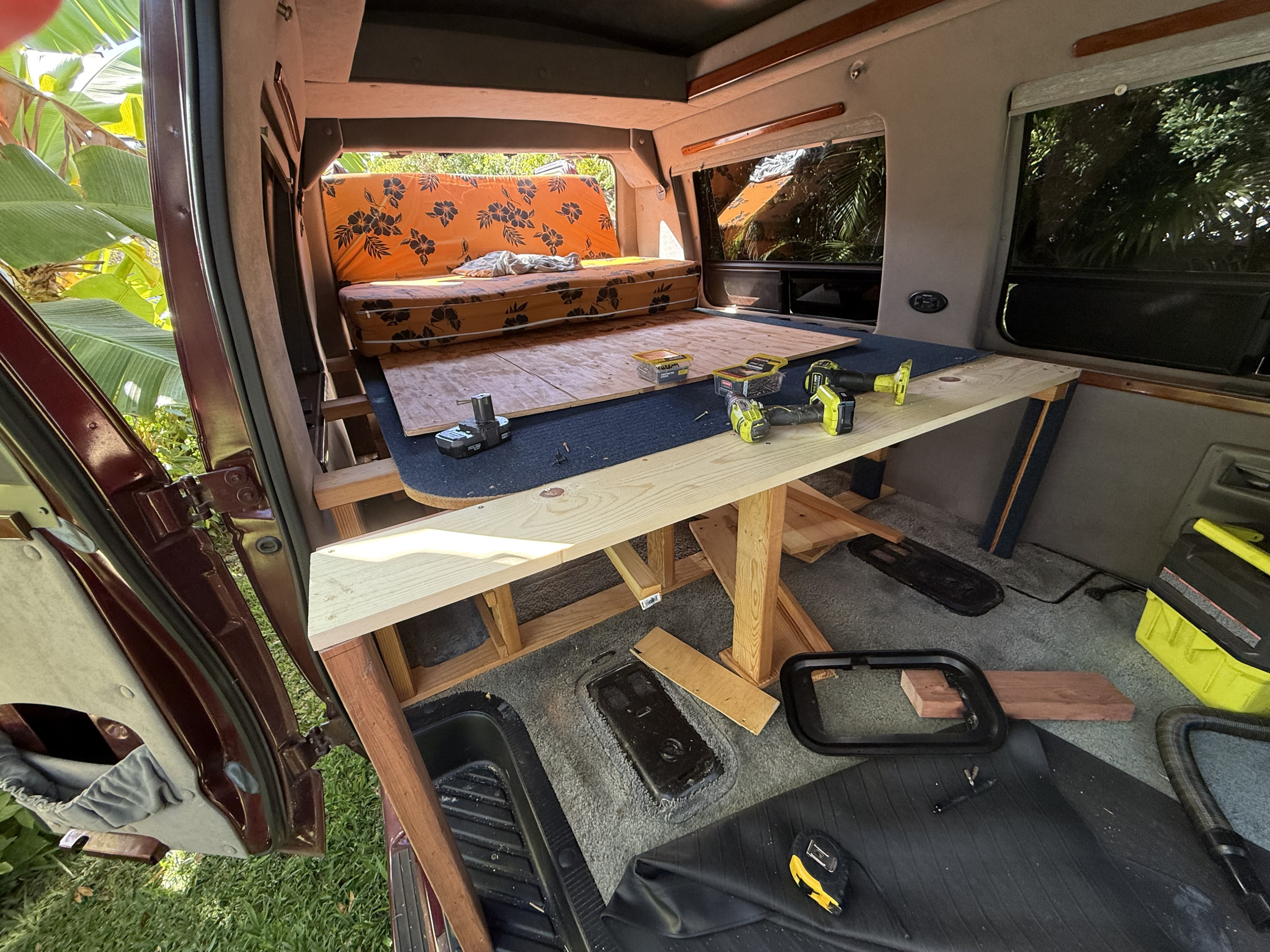Van conversion in progress: a wooden bed frame and table being built in the interior. Tools scattered, ready for an RV rental build.. Ford Econoline Club Wagon 2005