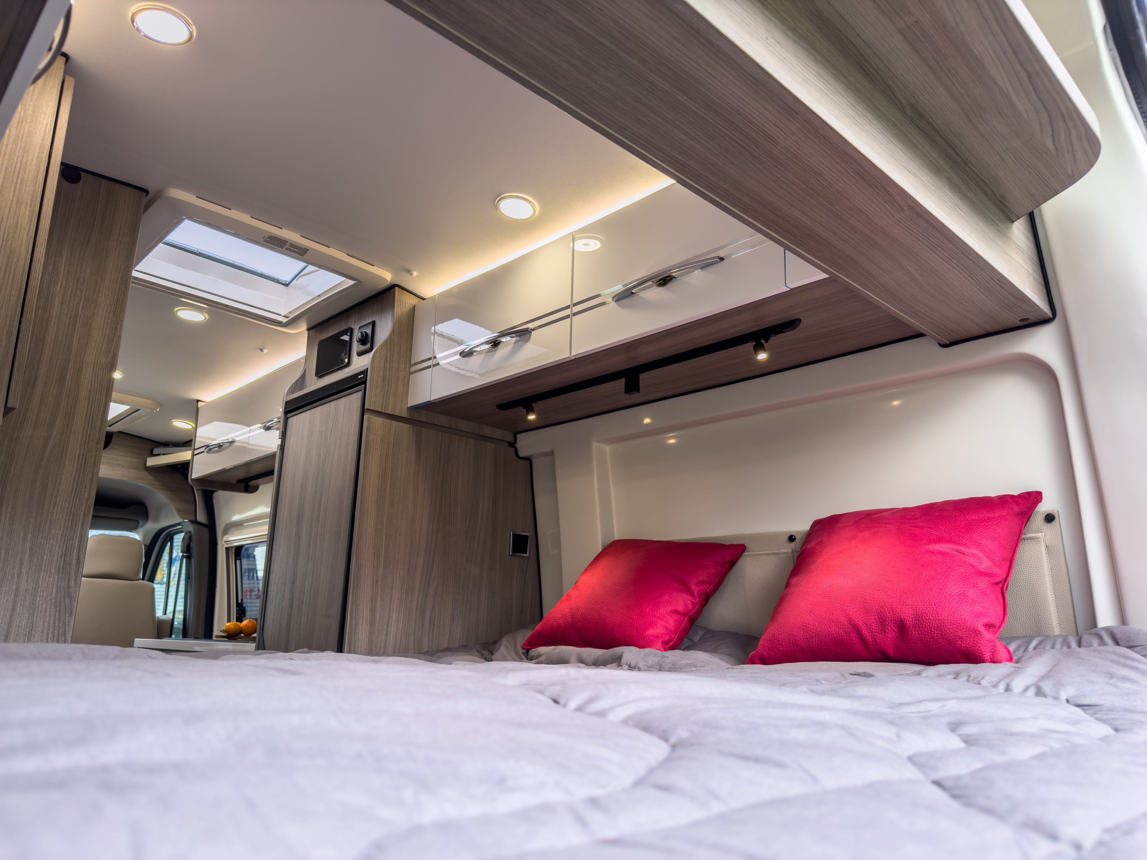 Cozy RV rental bedroom featuring a plush bed, vibrant pink pillows, overhead cabinets, and bright ceiling lights for comfort.. Randger R621 2025