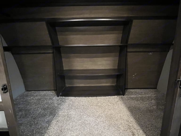 Empty dark wood closet/storage in an RV rental, featuring shelves, hanging rods, and gray carpeted floor.. Grand Design Reflection 2020