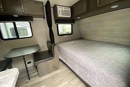 RV rental: Cozy interior featuring a bed, dinette with table, overhead cabinets, and AC unit for comfortable travel.. Jayco Jay Flight SLX 2021