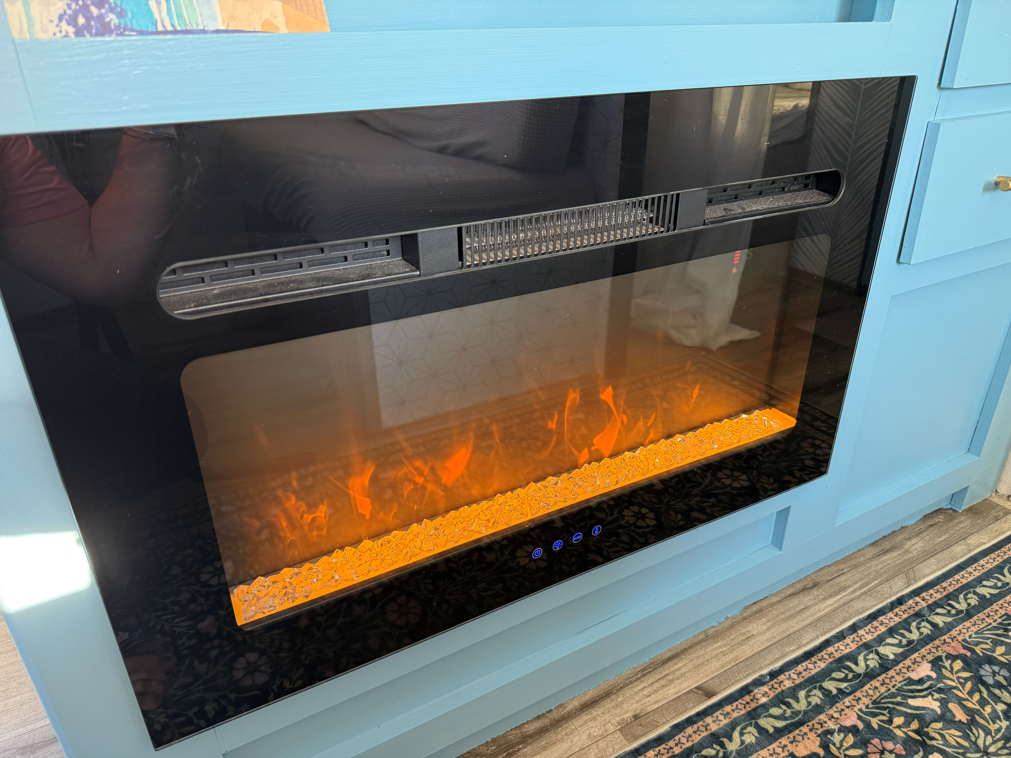 Cozy RV rental interior with a built-in electric fireplace glowing orange, set in light blue cabinetry for warmth and ambiance.. Dutchmen Coleman Lantern LT 2024