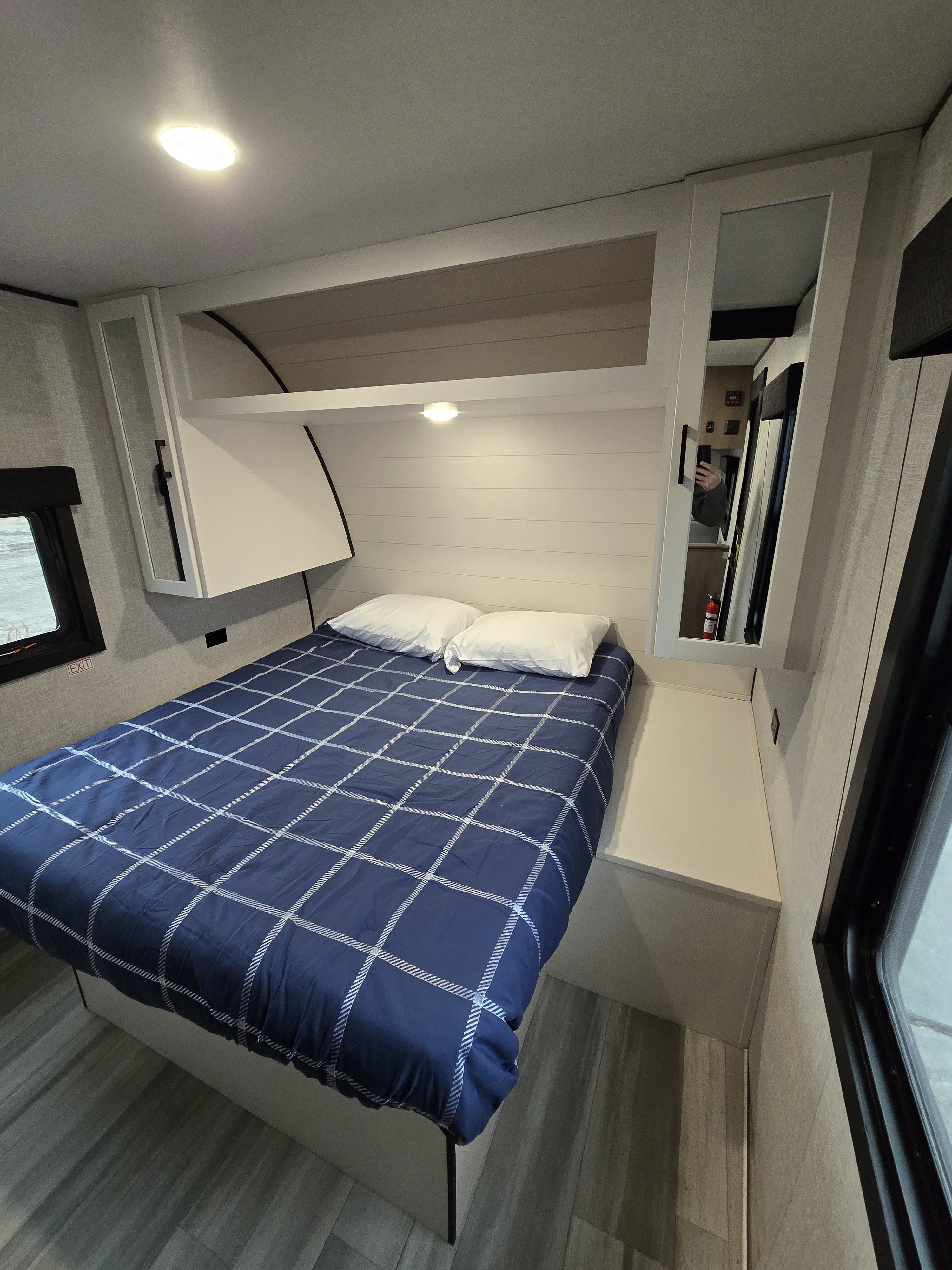 Cozy rv rental bedroom featuring a blue plaid bed, white pillows, overhead storage, and a side window for compact living.. Starcraft RV 26BH 2025