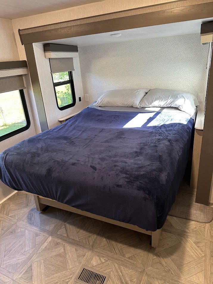 Cozy RV rental bedroom featuring a comfy bed with a blue blanket, pillows, and bright windows with scenic views.. Salem 36VBDS 2023