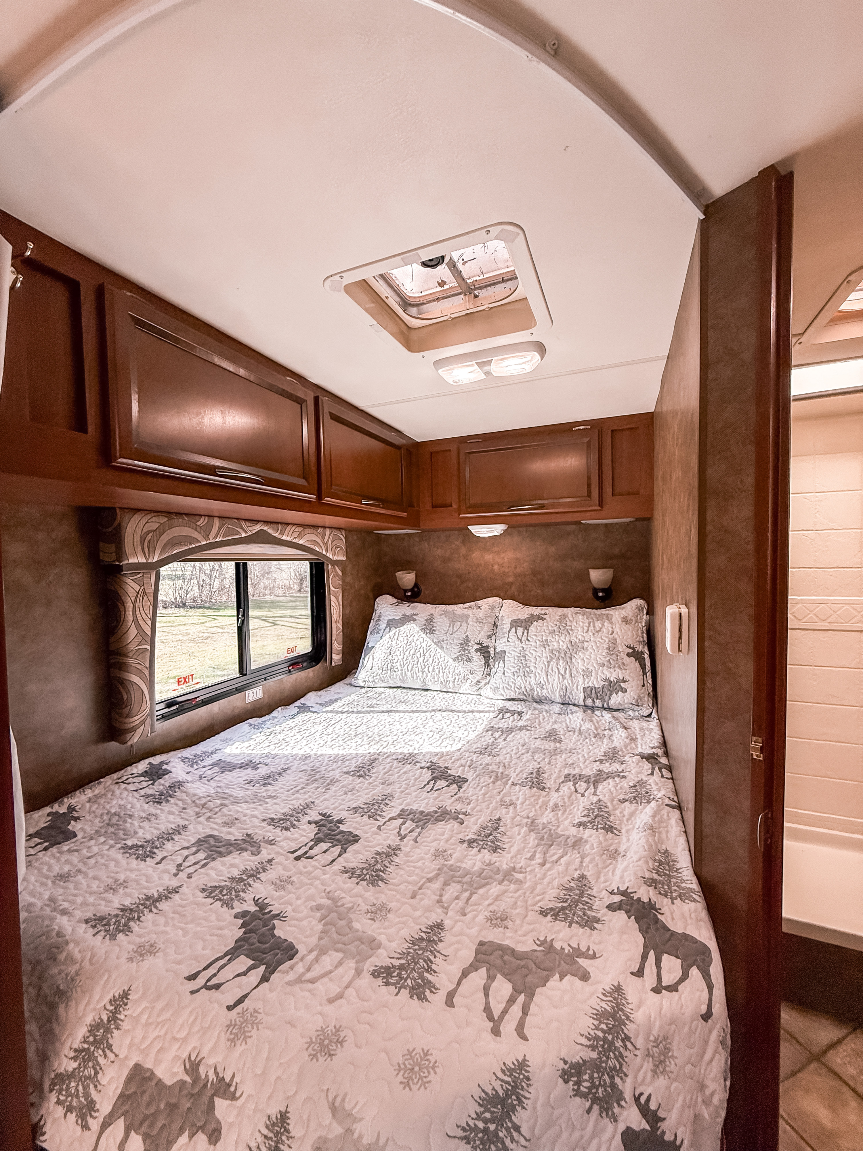 Inside an RV rental, a comfy bedroom features a bed with a moose quilt, overhead storage, and a large window.. Thor Motor Coach Chateau 2013