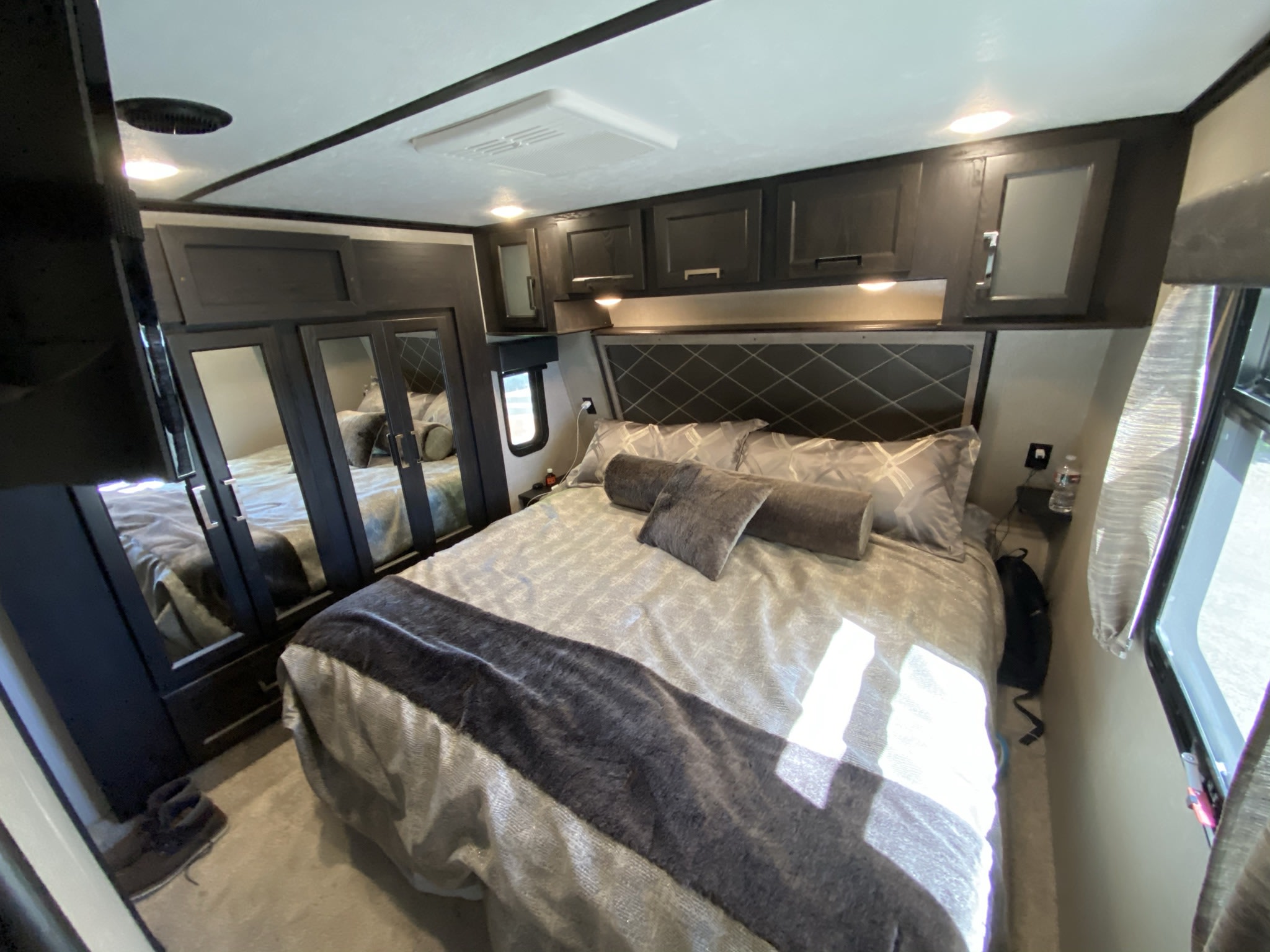 Experience comfort in this modern RV rental bedroom, featuring a large bed, dark wood cabinetry, and a mirrored wardrobe.. Keystone Fuzion 2018