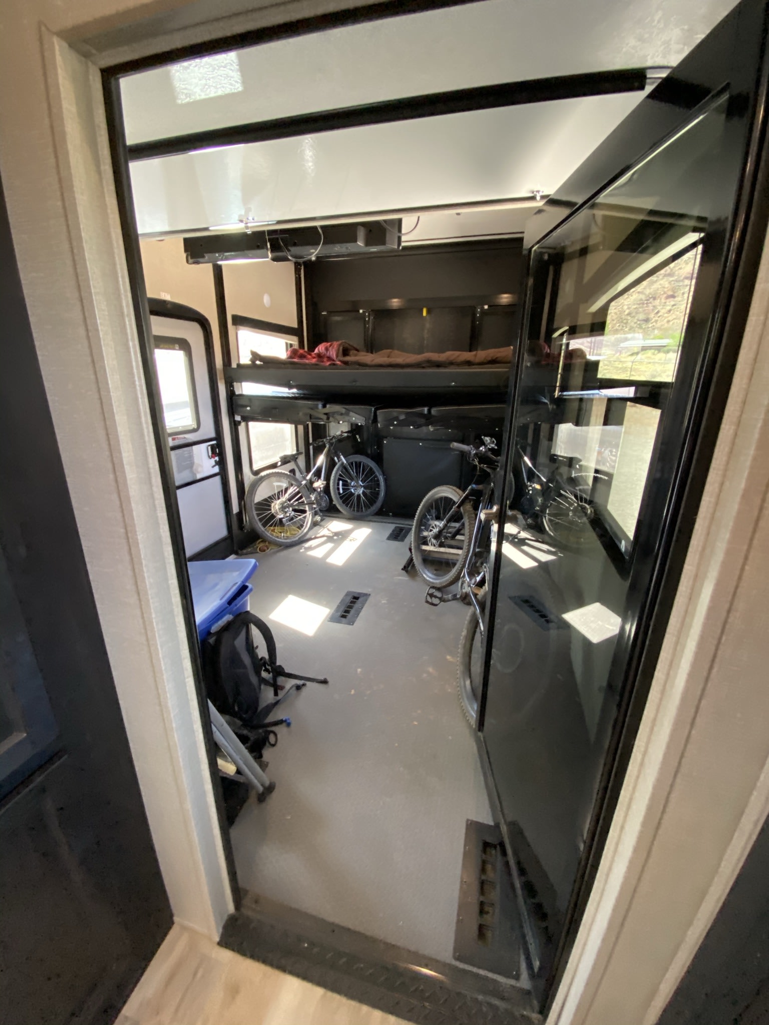 Inside an RV rental toy hauler garage, showing two bikes, bunk beds, and a side door, ready for adventure.. Keystone Fuzion 2018