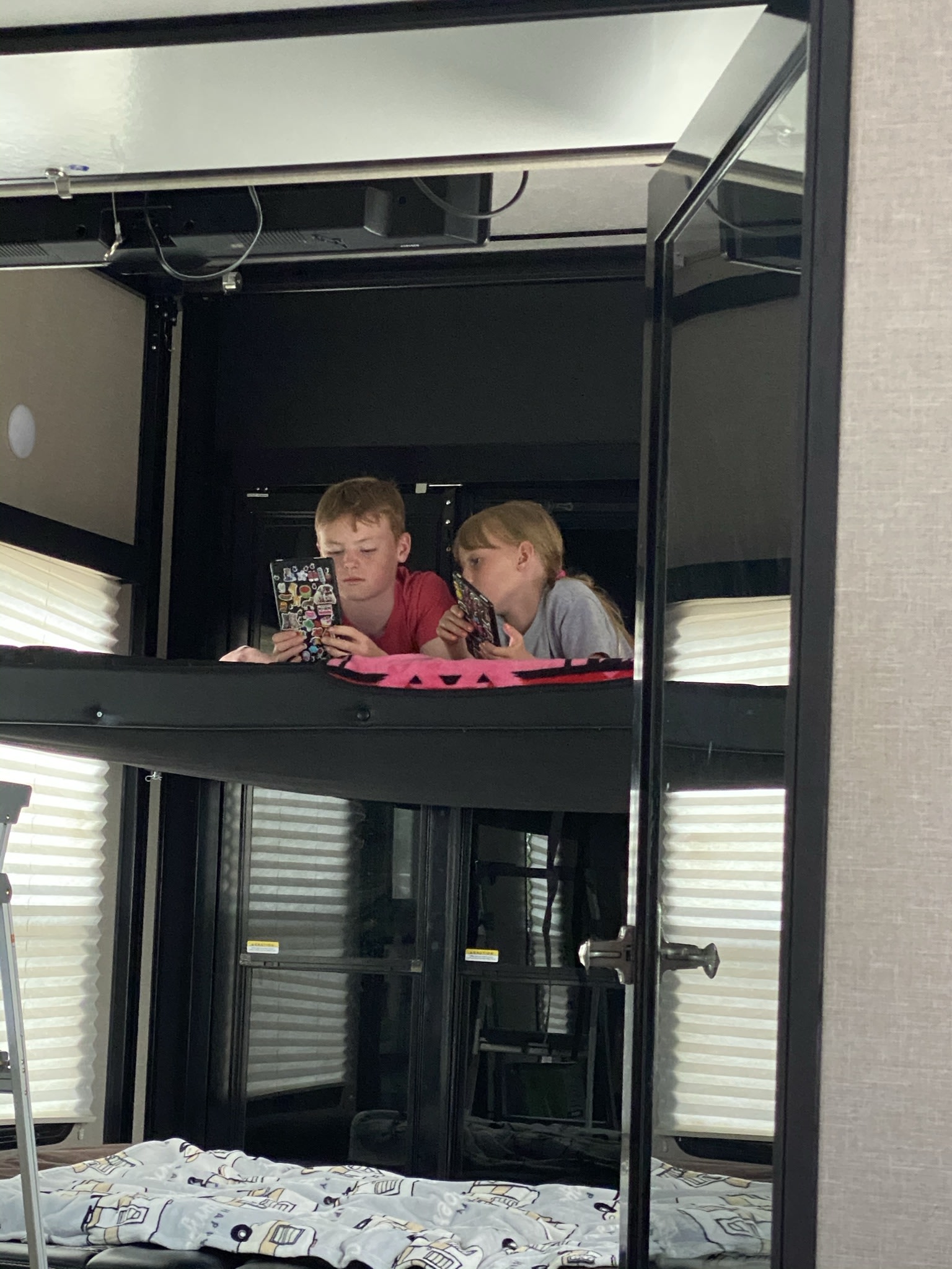 Kids relaxing in bunk beds in an RV rental, looking at tablets.. Keystone Fuzion 2018