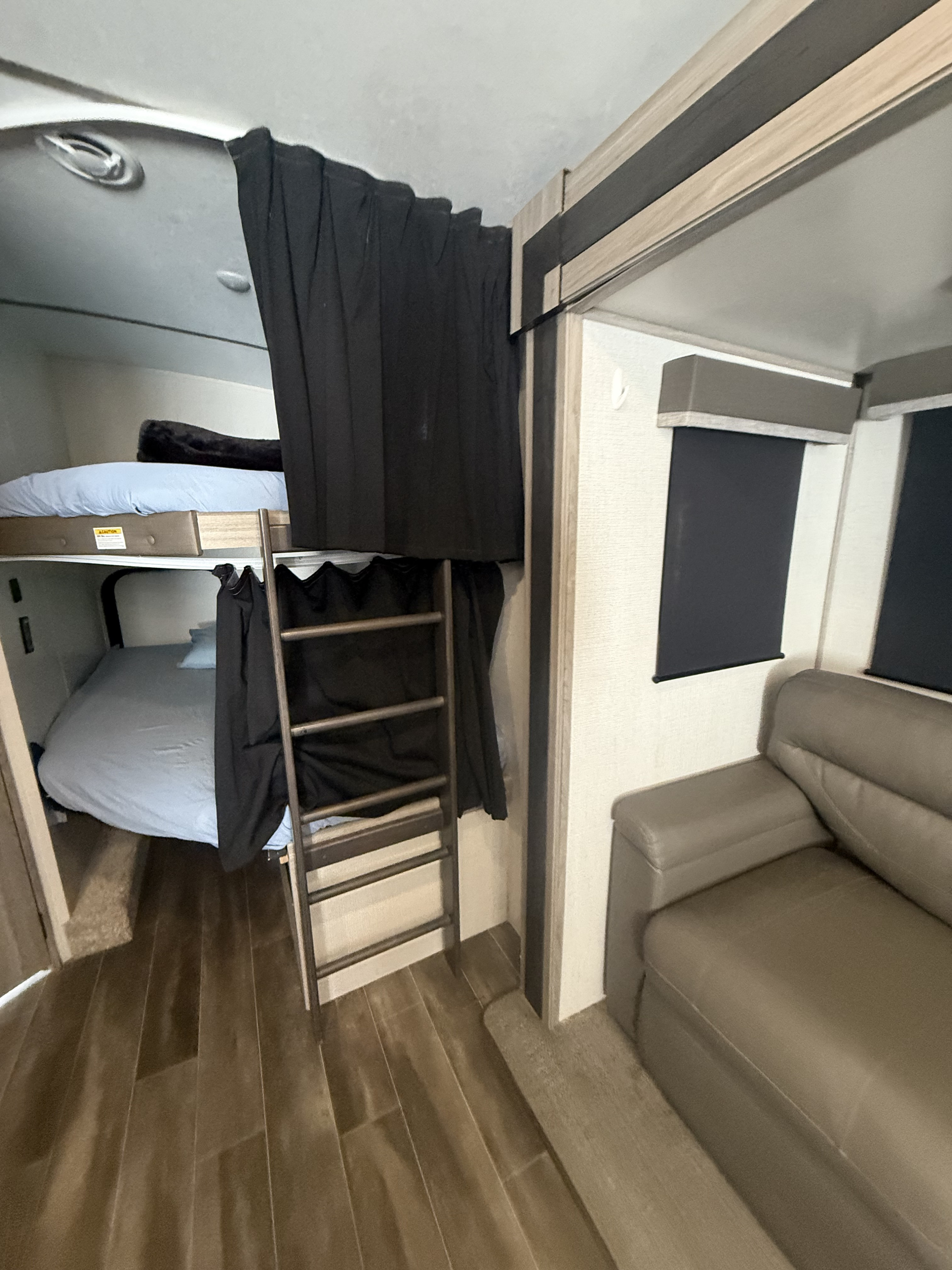 Inside an RV rental: dual bunk beds with privacy curtains and ladder, plus a comfy sofa. Ideal for travel families.. Passport 2950BH 2021