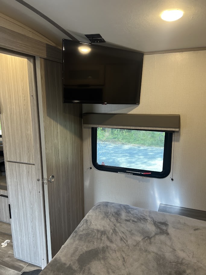 RV rental bedroom interior, featuring a wall-mounted TV, window with a blind, a cozy bed, and built-in storage.. Passport 2950BH 2021