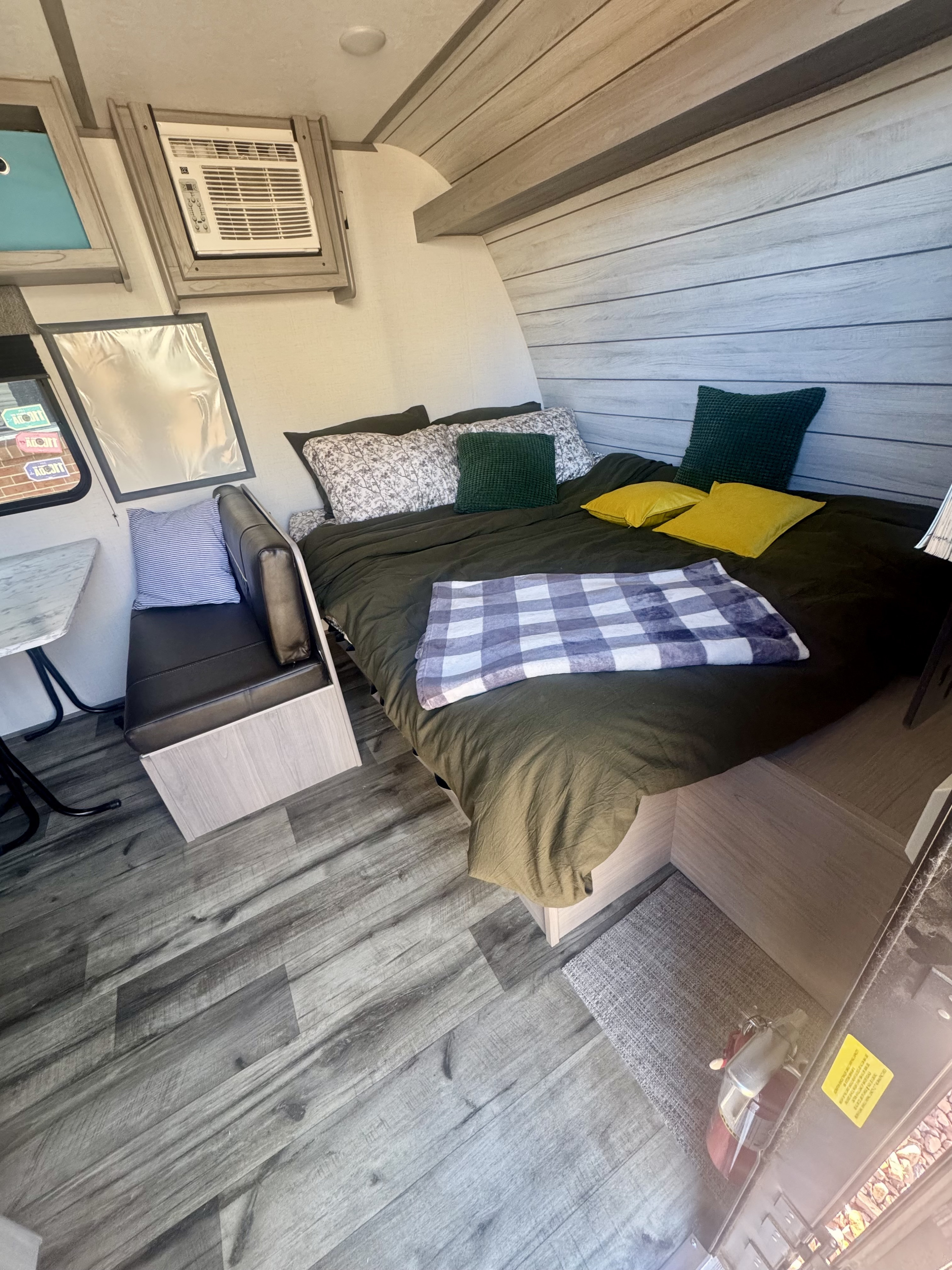 Cozy RV rental interior features a compact bed, dinette, and wall-mounted AC unit on wood-look flooring.. Keystone RV Coleman Lantern LT 17B 2024
