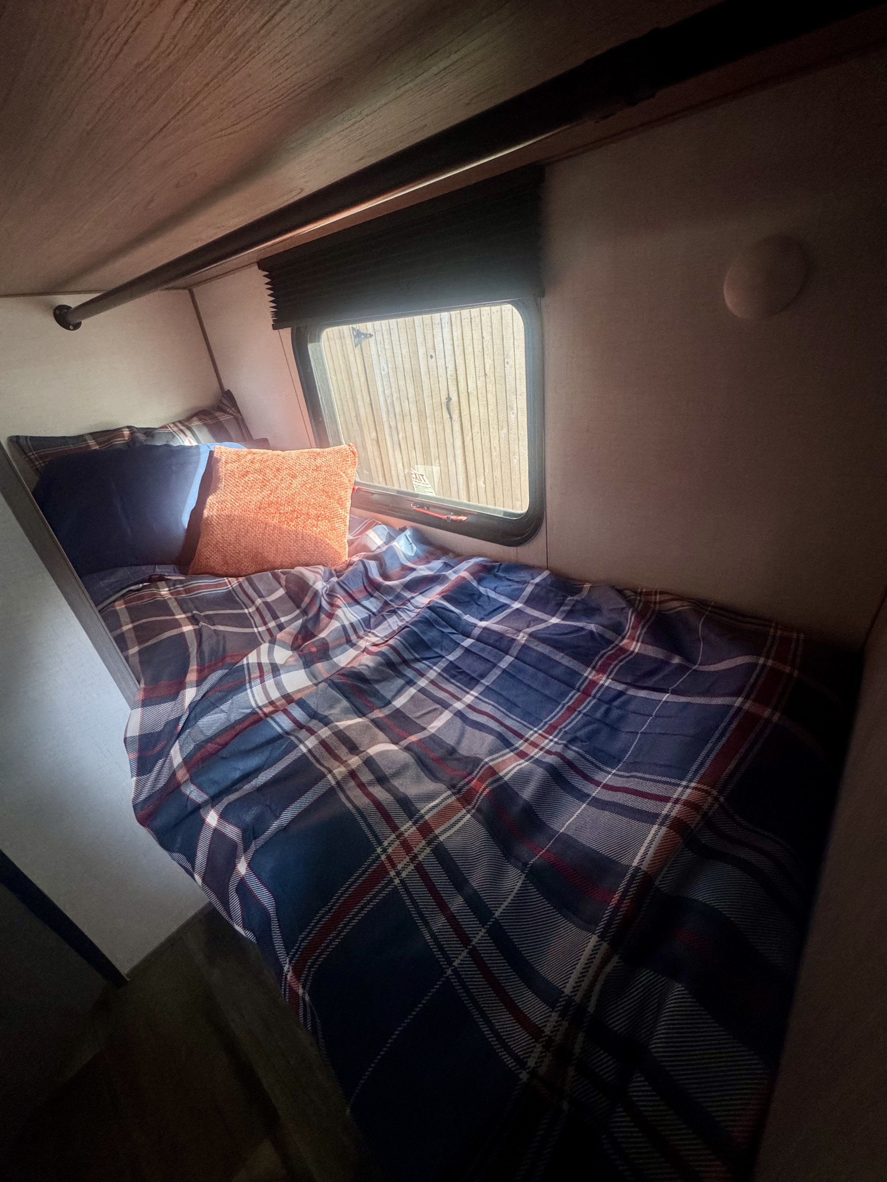 Cozy RV rental bunk bed with plaid bedding, blue and orange pillows, and a window looking out. RV interior.. Keystone RV Coleman Lantern LT 17B 2024