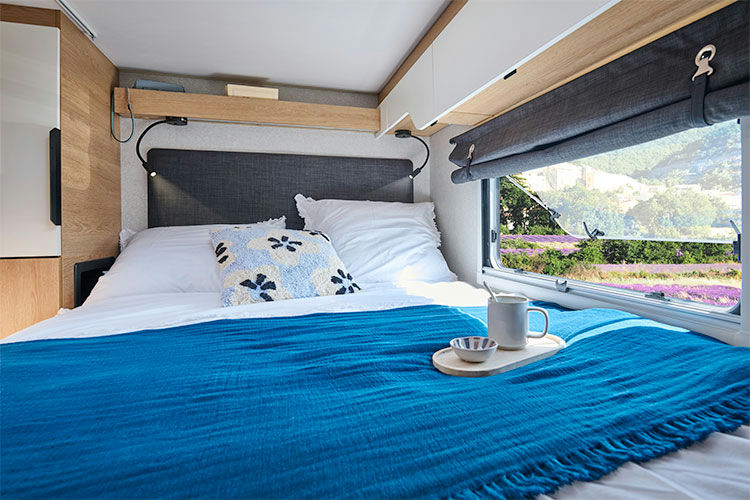 Experience comfort in this RV rental bedroom: cozy bed, reading lights, and a window overlooking a vibrant lavender field.. Pilote A630G 2025