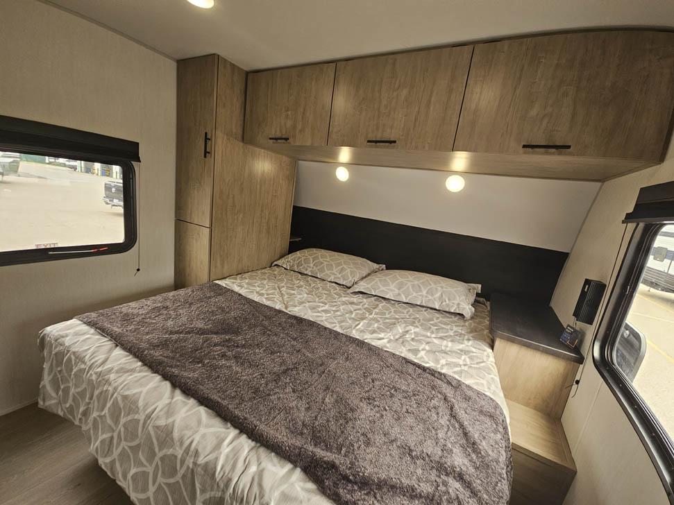 Cozy rv rental bedroom with a queen bed, patterned bedding, overhead storage, and a side window, shown from an interior angle.. Forest River Grey Wolf 29TE 2026