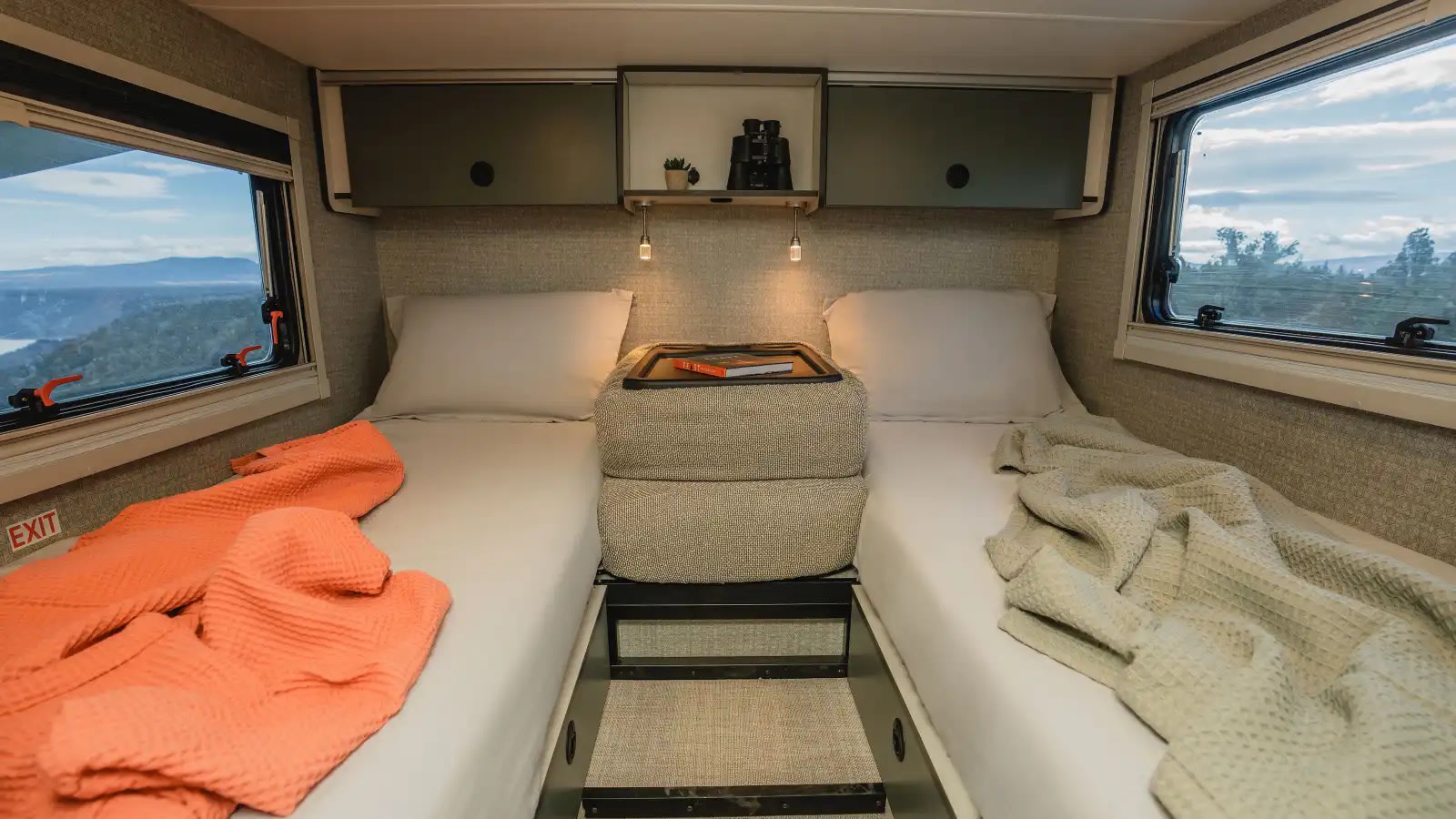 Cozy RV rental bedroom with twin beds, a central nightstand, overhead shelf with binoculars, and scenic window views.. Winnebago Ekko 2025