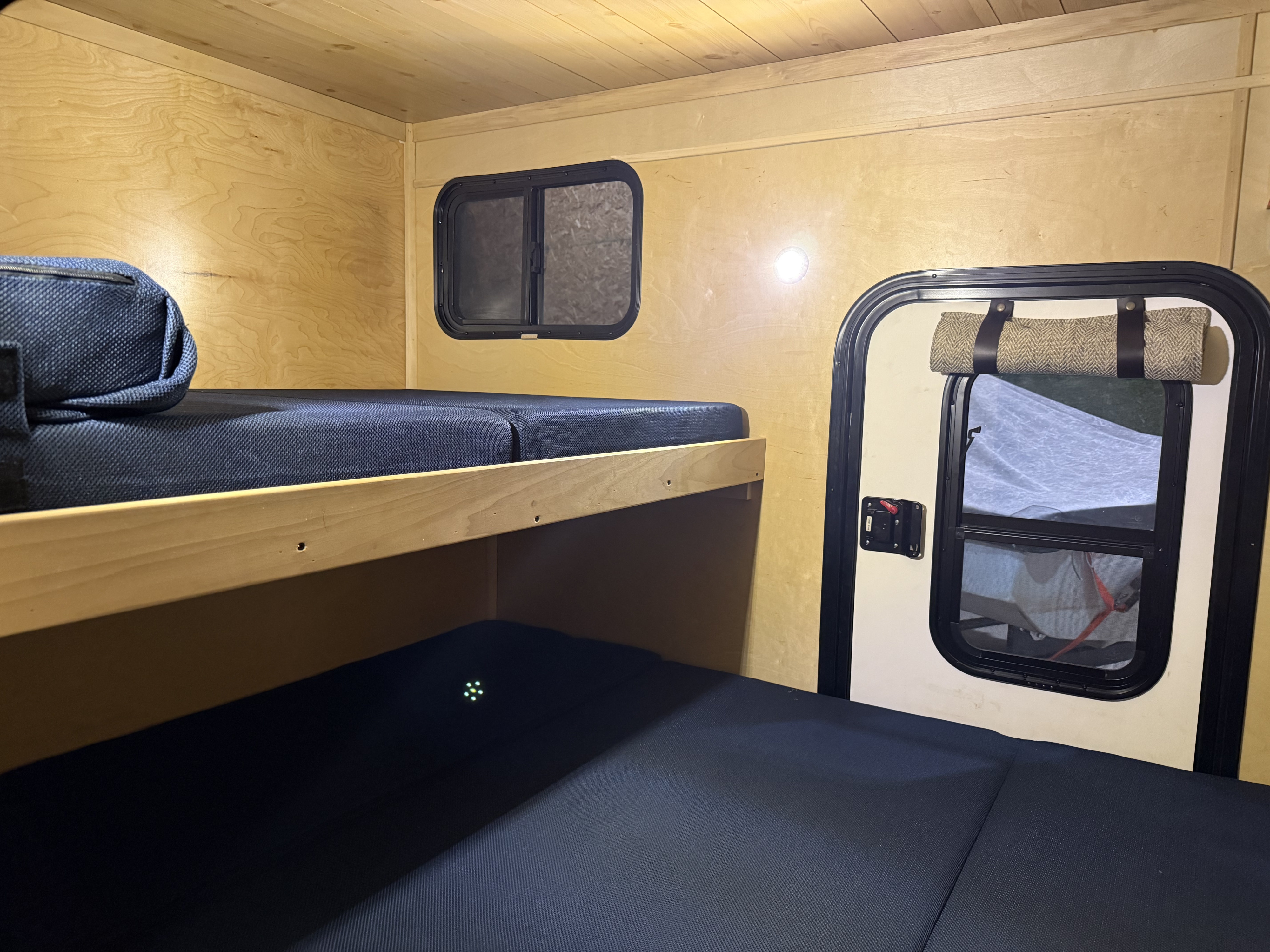 rv rental interior: wooden bunk beds with dark mattresses and windows offer a compact, cozy sleeping space for adventures.. CUSTOM ** GLAMPING - OFF GRID BUNK** 2021