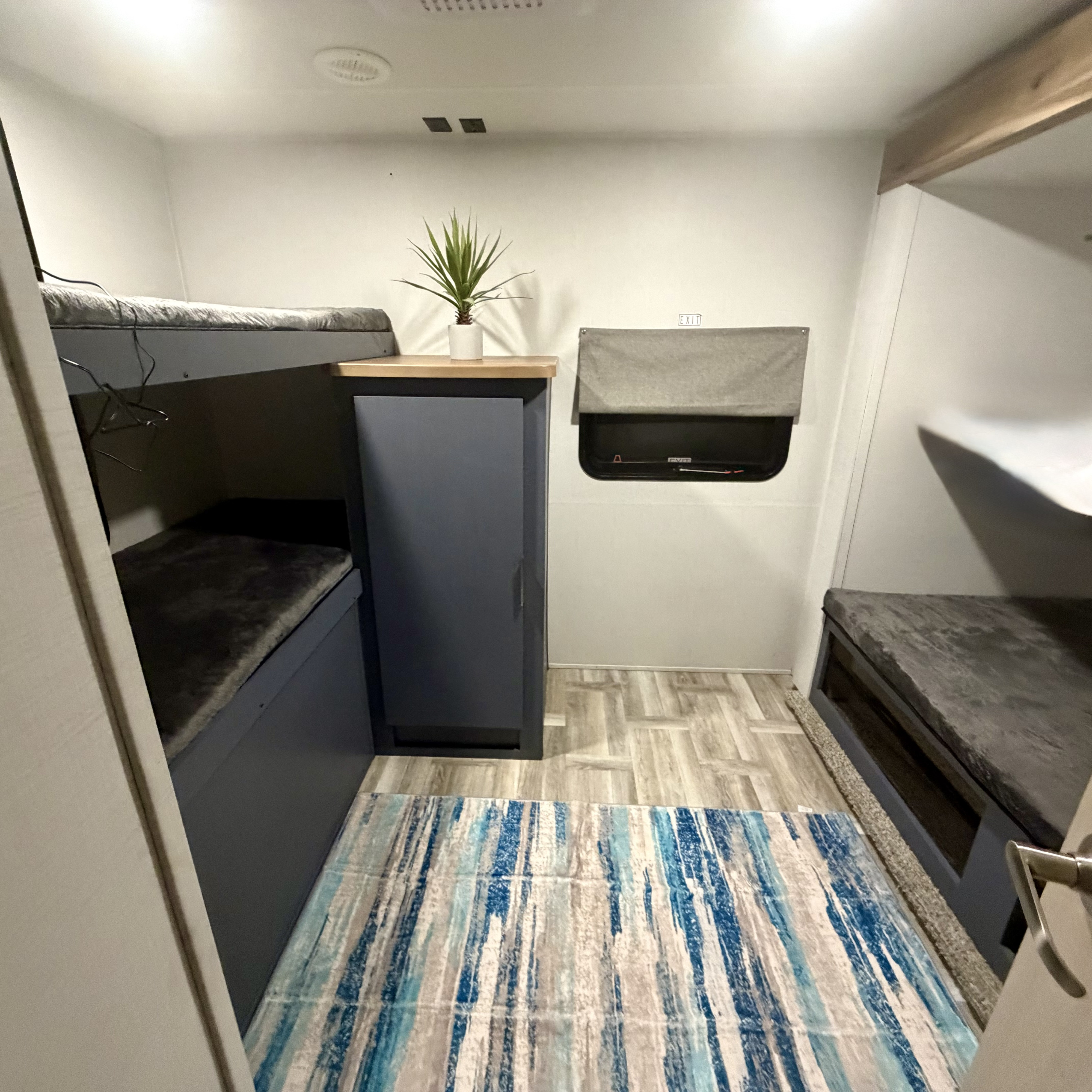 RV rental bunk room: grey bunks, blue cabinet, potted plant, and striped rug for compact travel.. Forest River Tracer Ultra Lite LE 2025