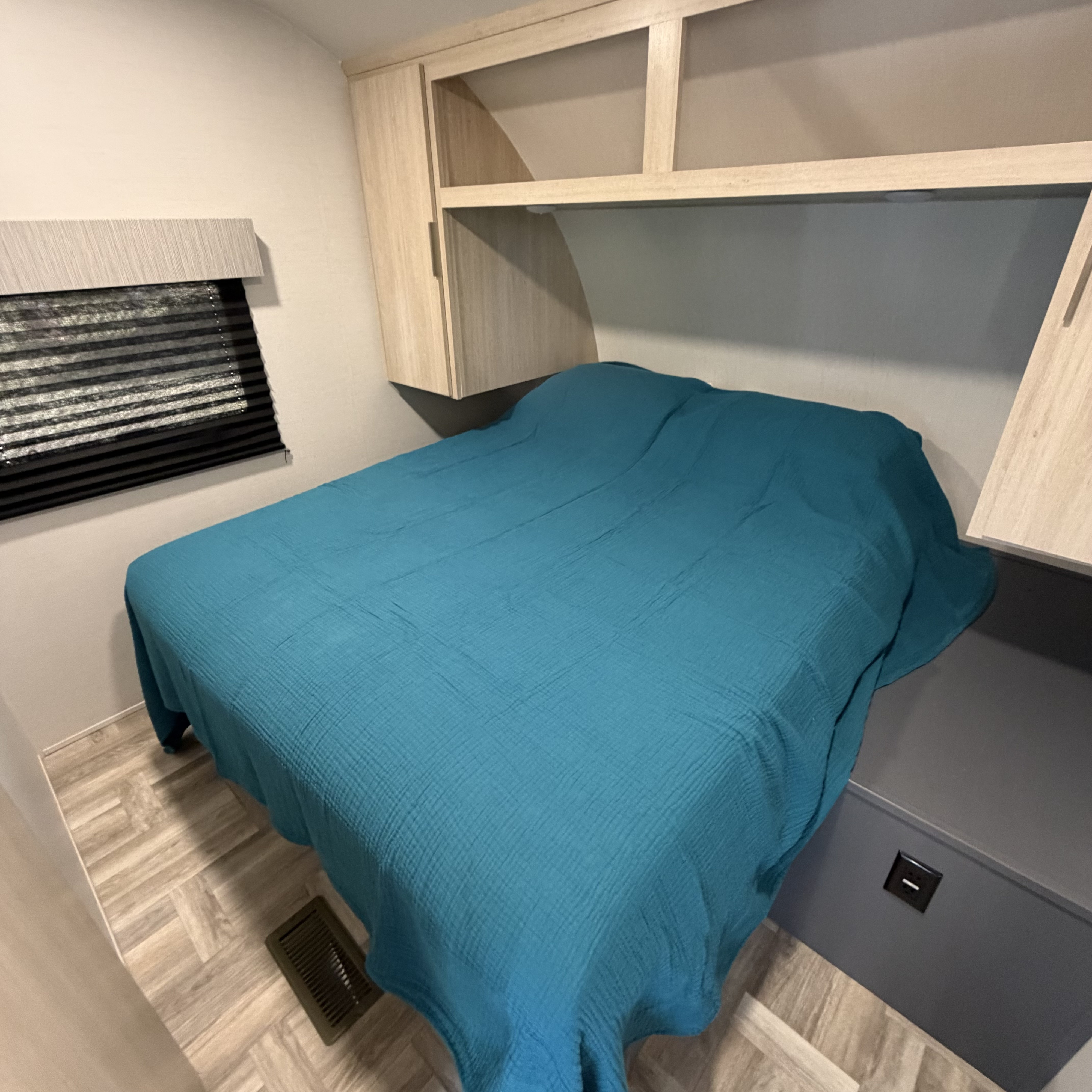 Inside an RV rental: a cozy bedroom with a teal bed, overhead storage, and window, perfect for your next adventure.. Forest River Tracer Ultra Lite LE 2025