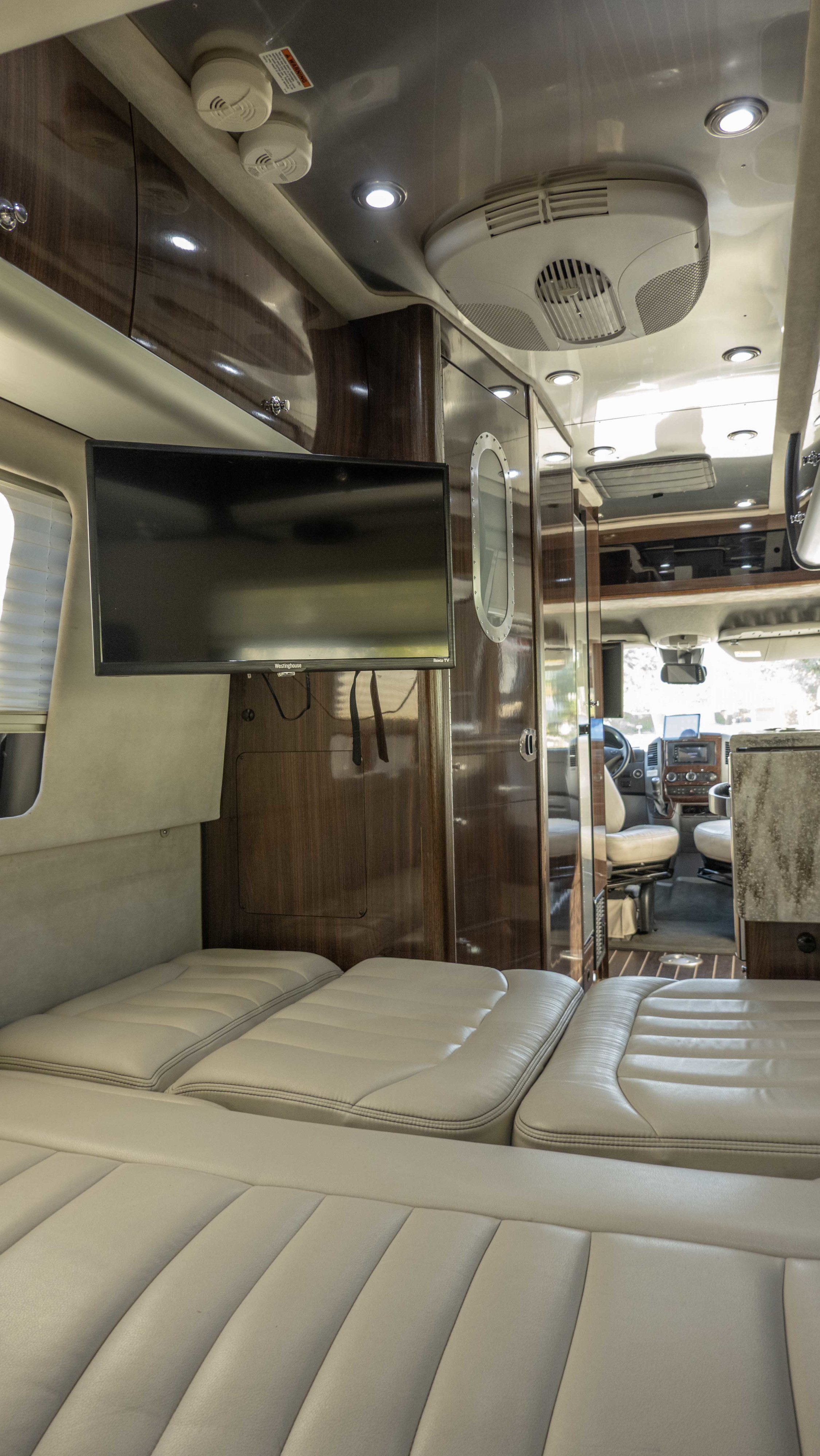 View of a modern rv rental interior with plush cream seating, a mounted TV, and sleek wood cabinetry.. Airstream Interstate 2015