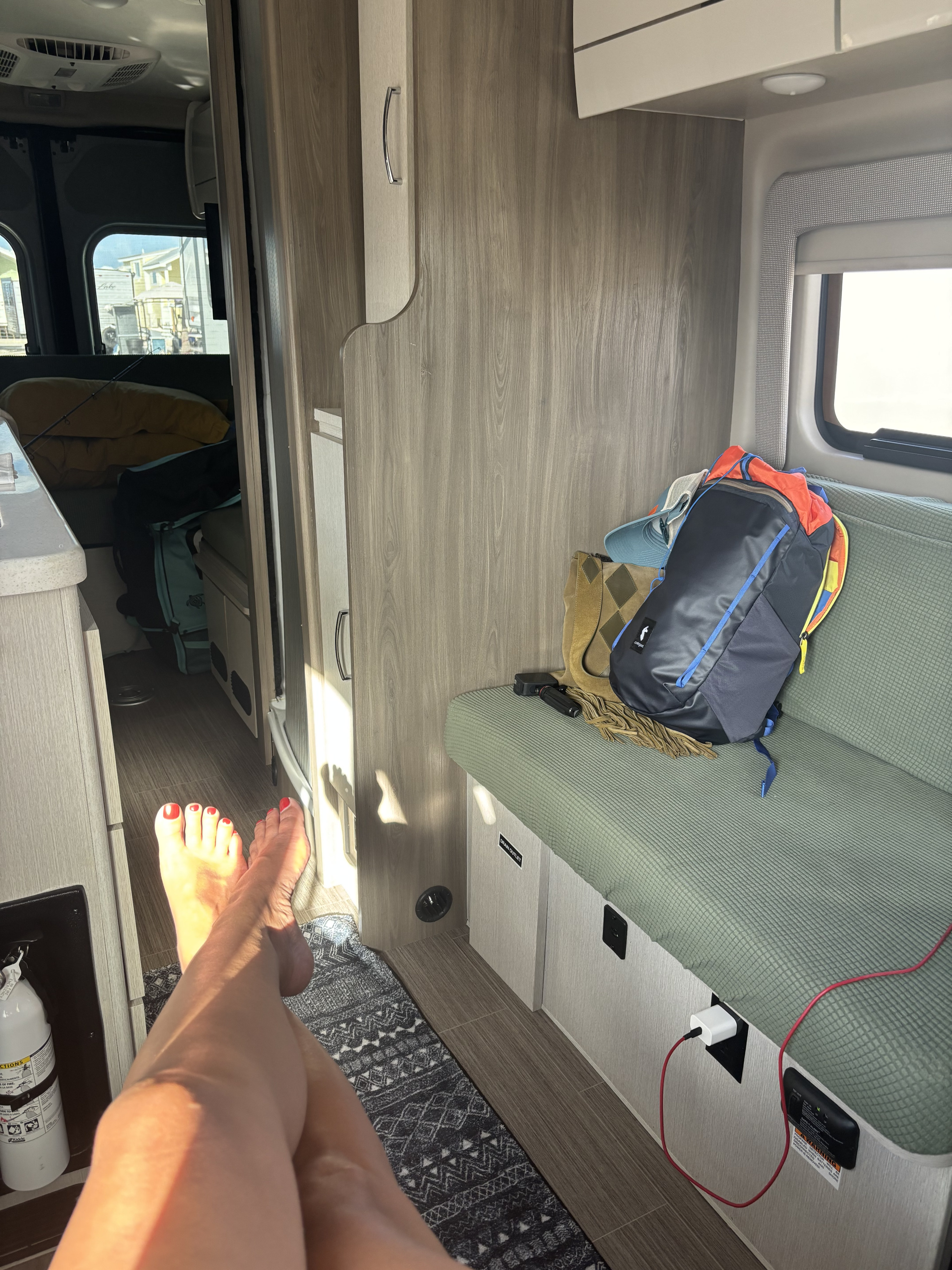 Sun-drenched RV rental interior with bare feet, green seating, storage, and a charging station. Ideal for travel comfort.. Thor Tellaro 2023