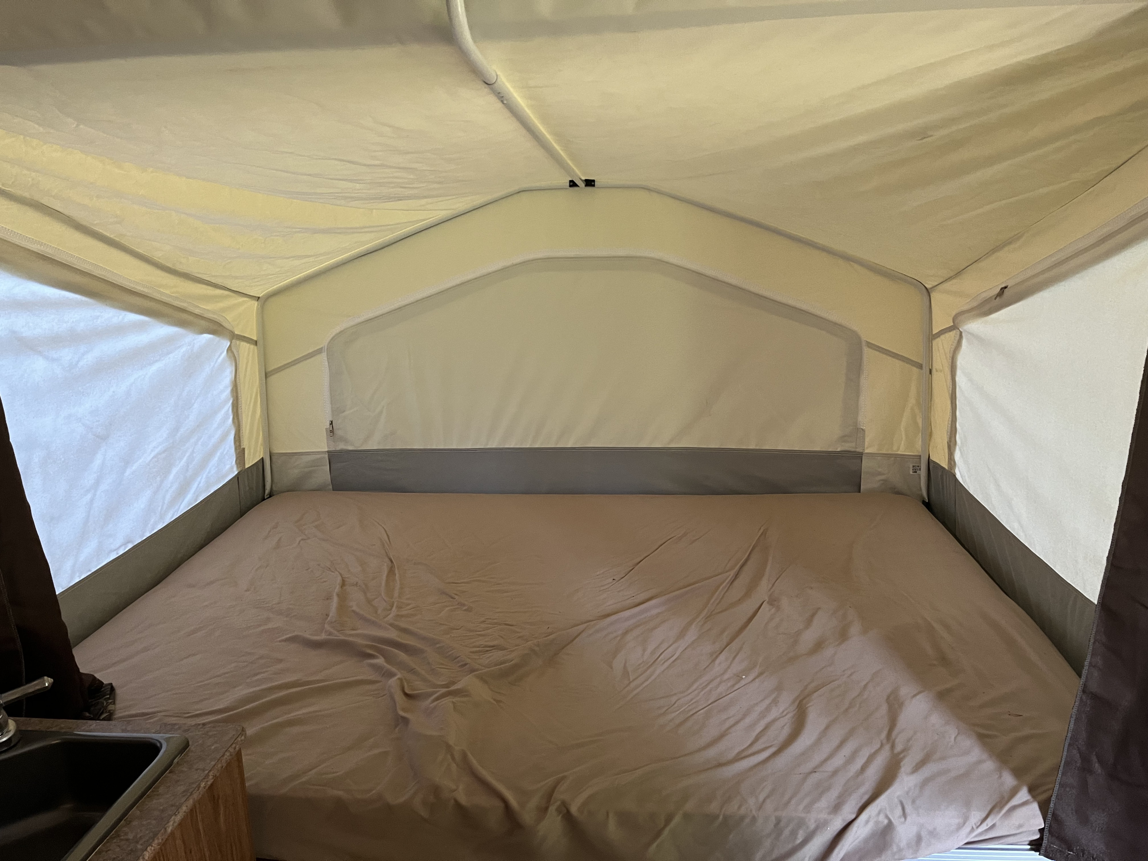 Inside an RV rental pop-up, revealing a cozy bed with brown sheets, light canvas walls, and a small sink area.. Forest River Rockwood 2012