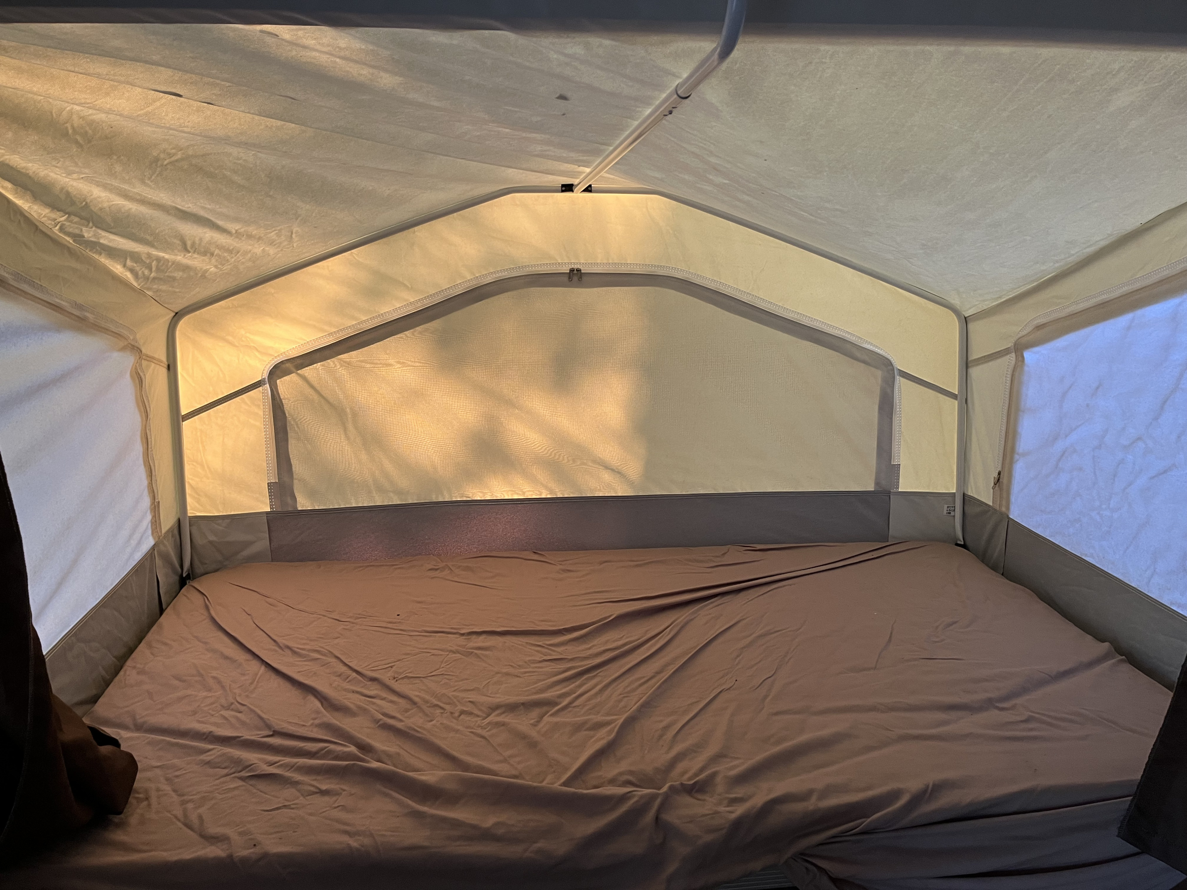 Inside a cozy RV rental pop-up camper: a bed with brown sheets and mesh windows, perfect for camping relaxation.. Forest River Rockwood 2012