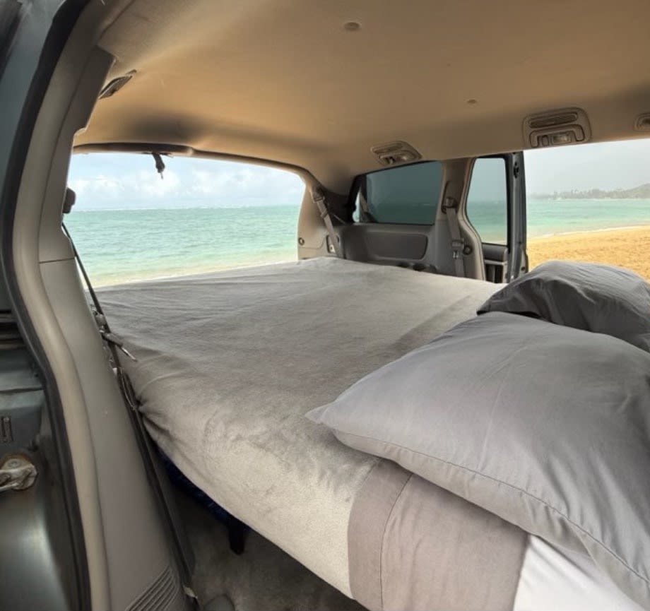 RV rental: Inside a customized van, a comfortable bed offers direct views of a sandy beach and blue ocean.. Toyota Sienna 2006