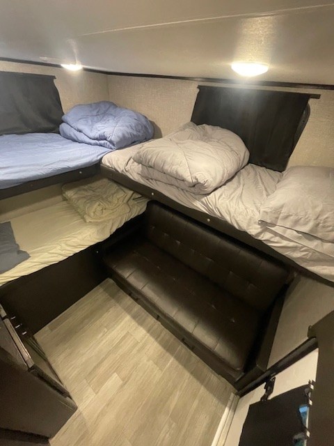 RV rental bunkhouse interior: multiple beds with light bedding, a brown futon, and wood-look flooring.. Jayco Jay Feather 2021