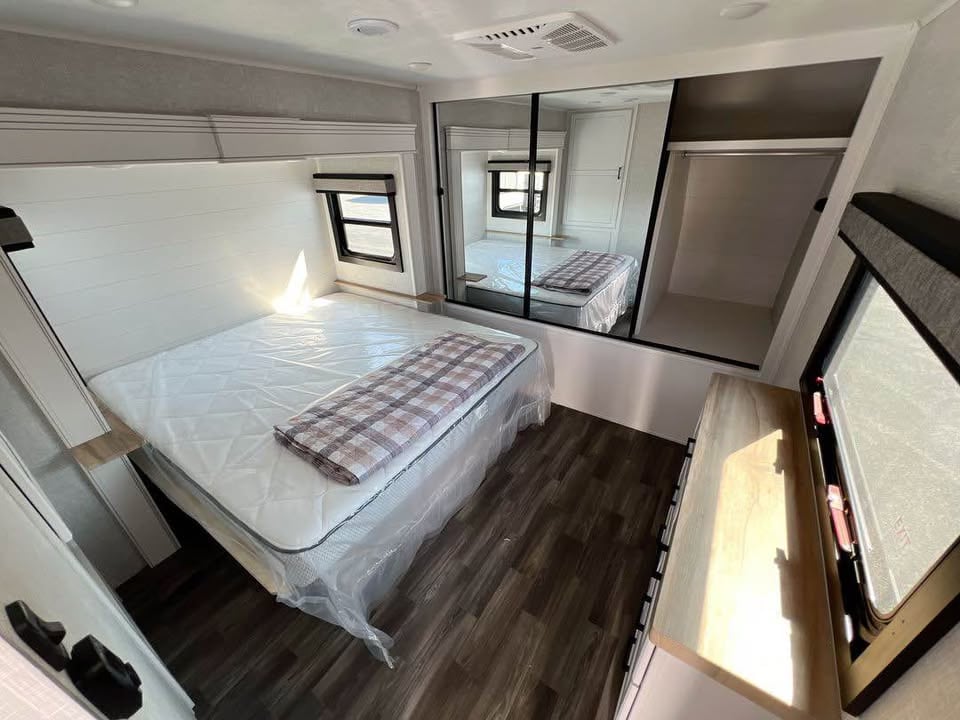 Clean RV rental bedroom with a queen bed, mirrored closet, and window for comfortable travel.. Jayco Eagle 2024