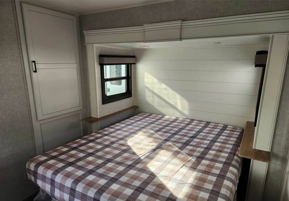 Inviting RV rental bedroom with a checkered bed, shiplap wall, window, and built-in storage cabinet.. Jayco Eagle 2024