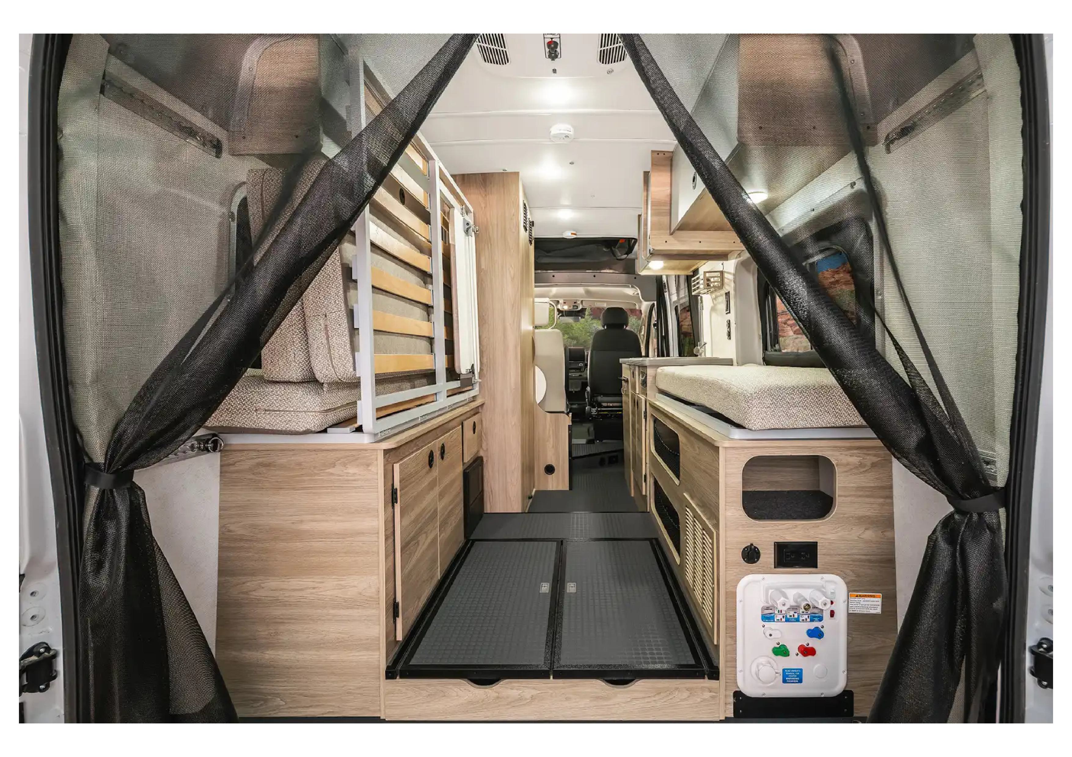 RV rental interior seen from the rear, featuring mesh screens, light wood cabinetry, beds, and the driver's seat forward.. Airstream Rangeline 2023