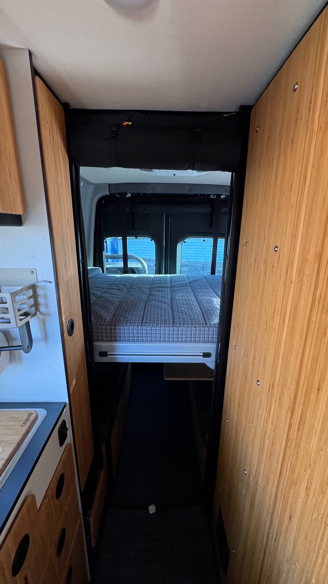Step into this RV rental! A compact interior featuring a comfortable raised bed, kitchen prep area, and sleek wood paneling.. Winnebago Revel 2023