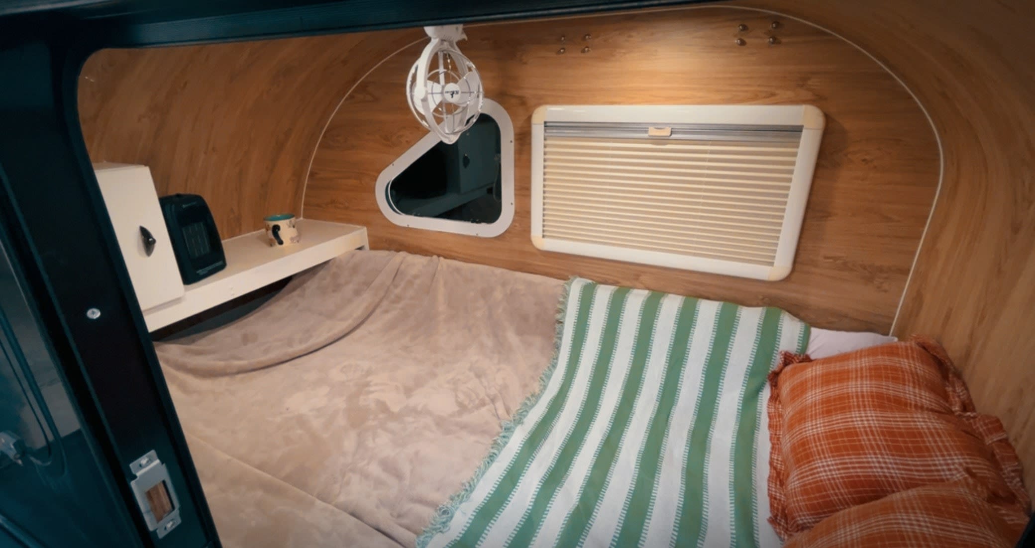 Compact rv rental interior showing a cozy sleeping area with wood paneling, a bed, heater, fan, and windows.. Ecocamper Vehicle Co. Eco camper 2023