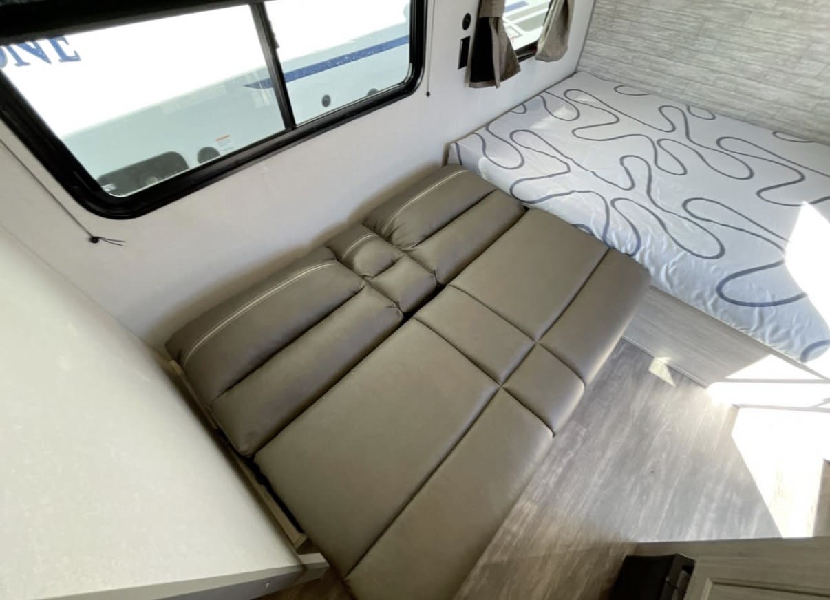 RV rental interior: convertible dinette transforms into a bed, plus a patterned bunk. Compact, cozy sleeping arrangements.. Forest River Aurora Aurora 2024