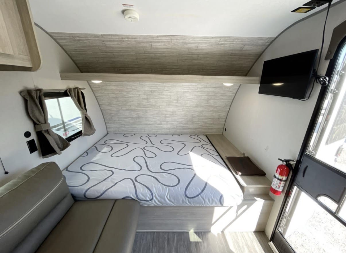 This RV rental offers a compact bedroom with a cozy bed, sofa, TV, window, and visible fire extinguisher for safety.. Forest River Aurora Aurora 2024