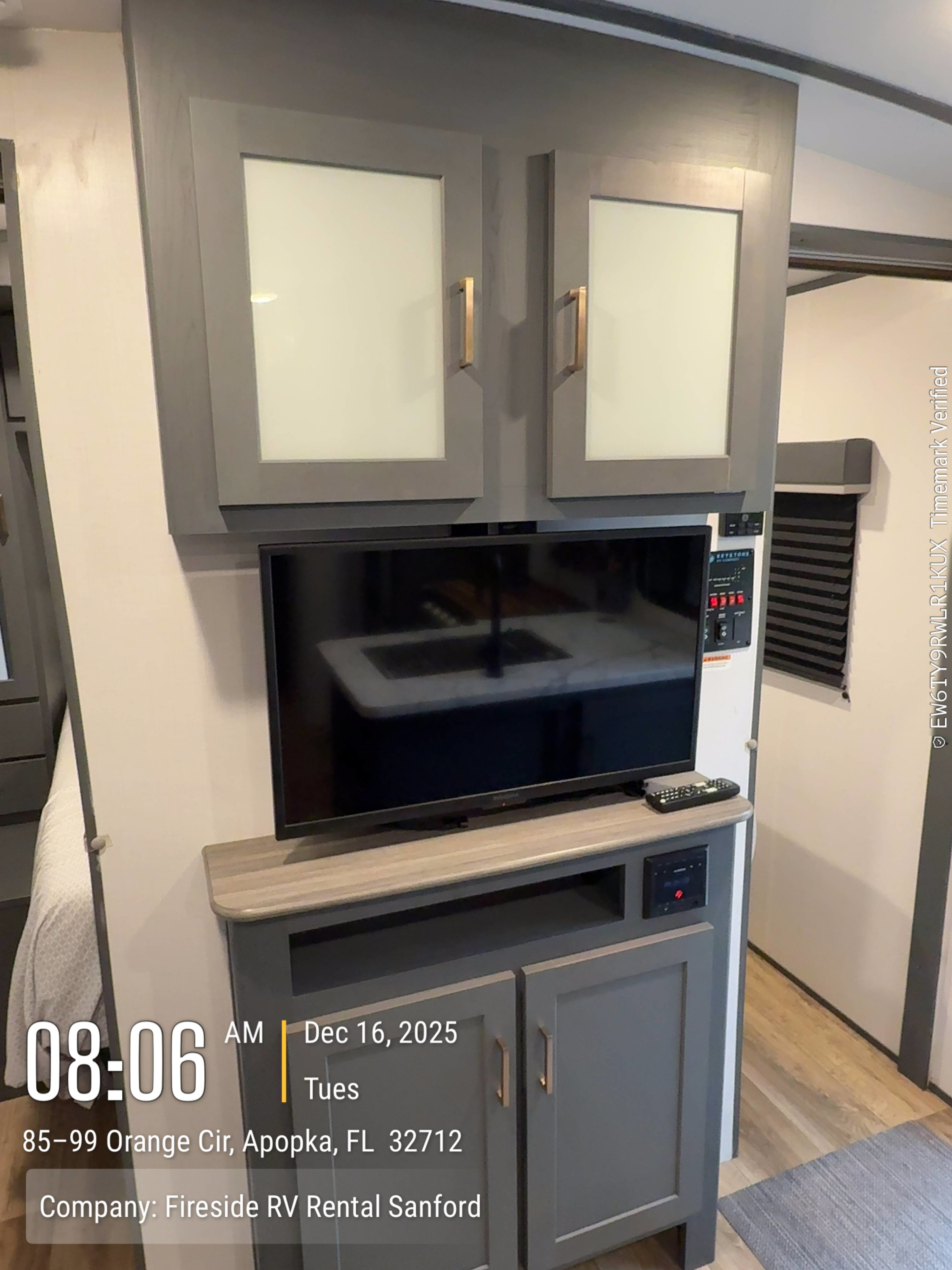 Interior view of an RV rental showing a TV, gray storage cabinets, and a control panel. Fireside RV Rental Sanford.. Keystone Bullet 2022