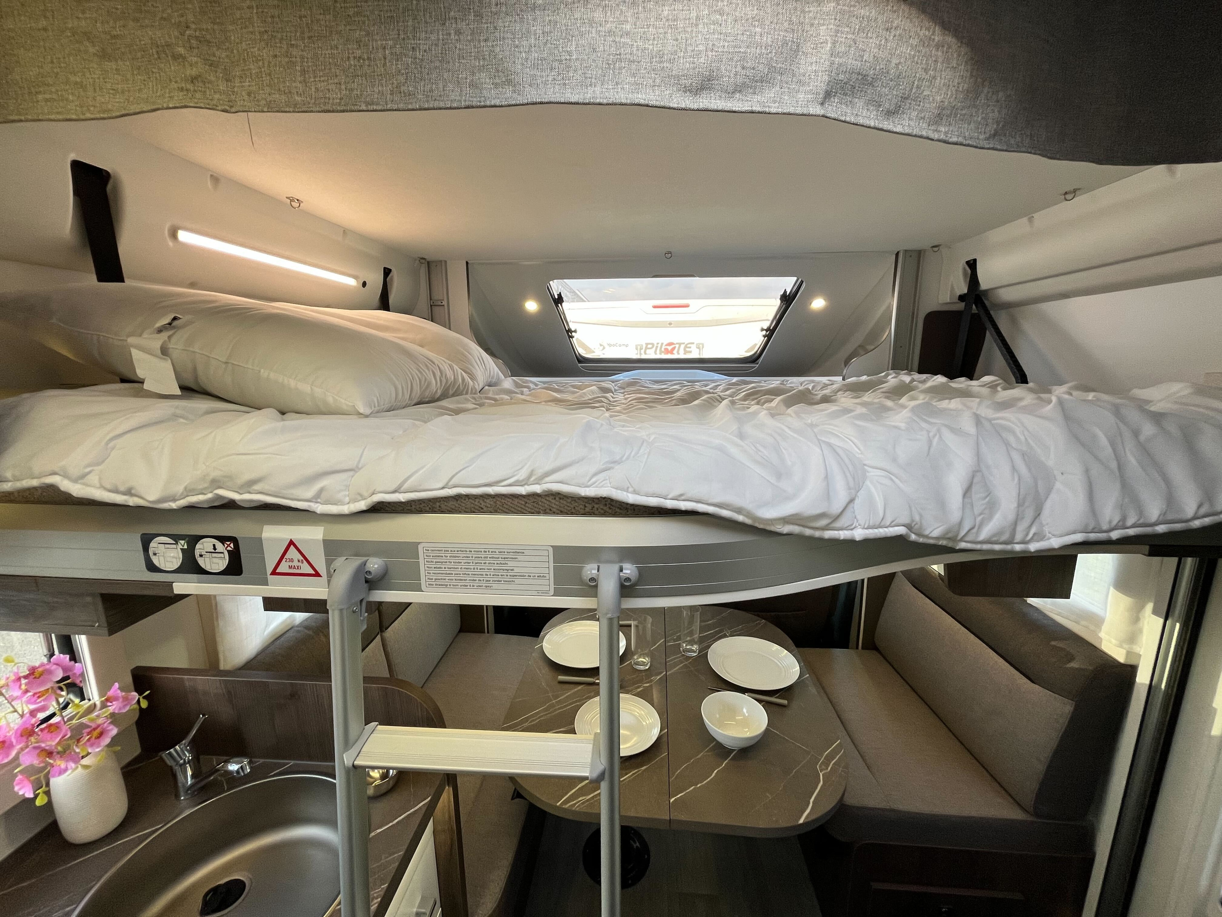 Bright rv rental interior featuring a cozy overhead bunk bed with a ladder, a set dinette below, and a compact kitchen sink area.. BENIMAR T 497 TESSORO 2025