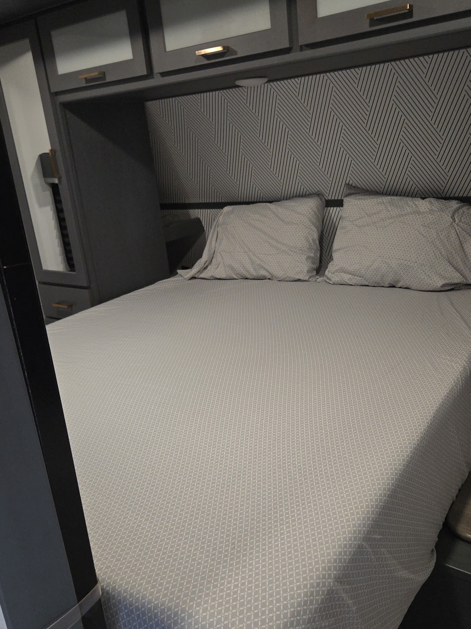 Modern RV rental: a compact bedroom features grey bedding, a geometric headboard, and sleek overhead cabinets.. Keystone Bullet 2022