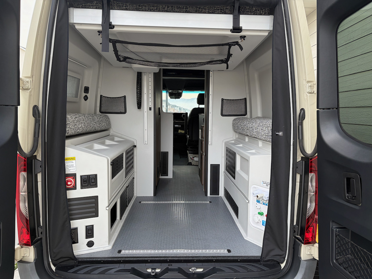 Open rear doors reveal a functional rv rental camper van interior with flexible seating and storage.. Tiffin GH1 2025
