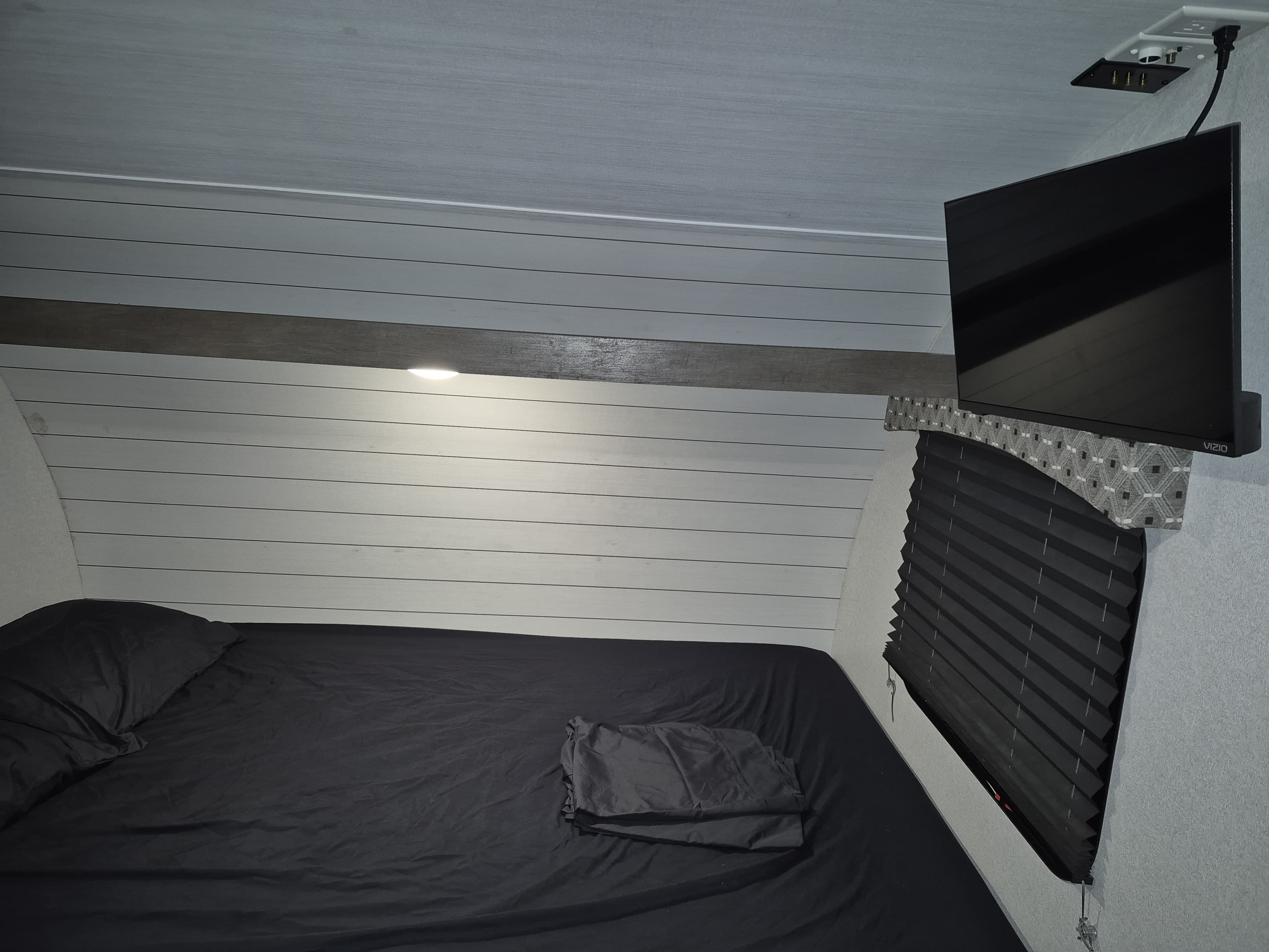 Cozy RV rental bedroom with black bed, wall-mounted TV, and pleated window shade. Perfect for a comfortable stay.. Forest River Sonoma 2020